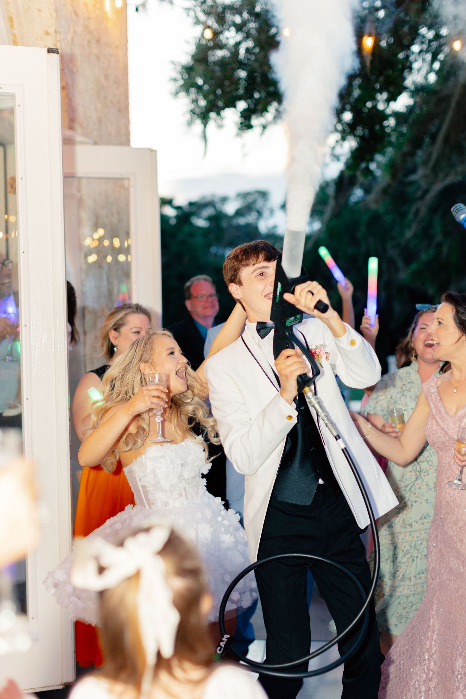Bride and groom celebrate at wedding reception with fog machine, glow sticks, and guests cheering in elegant outdoor venue, Bella Cosa