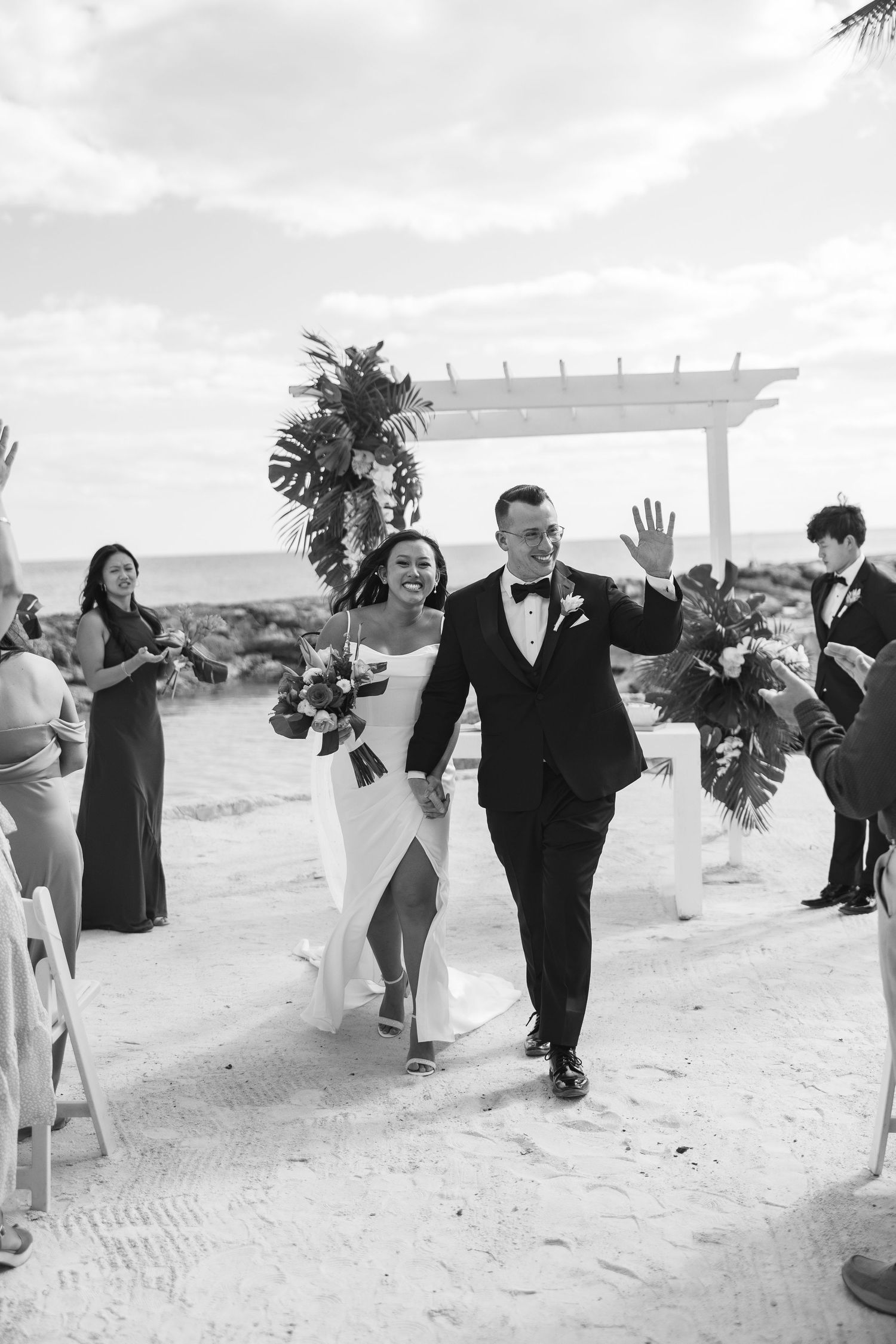 Black and white photo of a joyful couple walking down the aisle after their beach wedding ceremony.