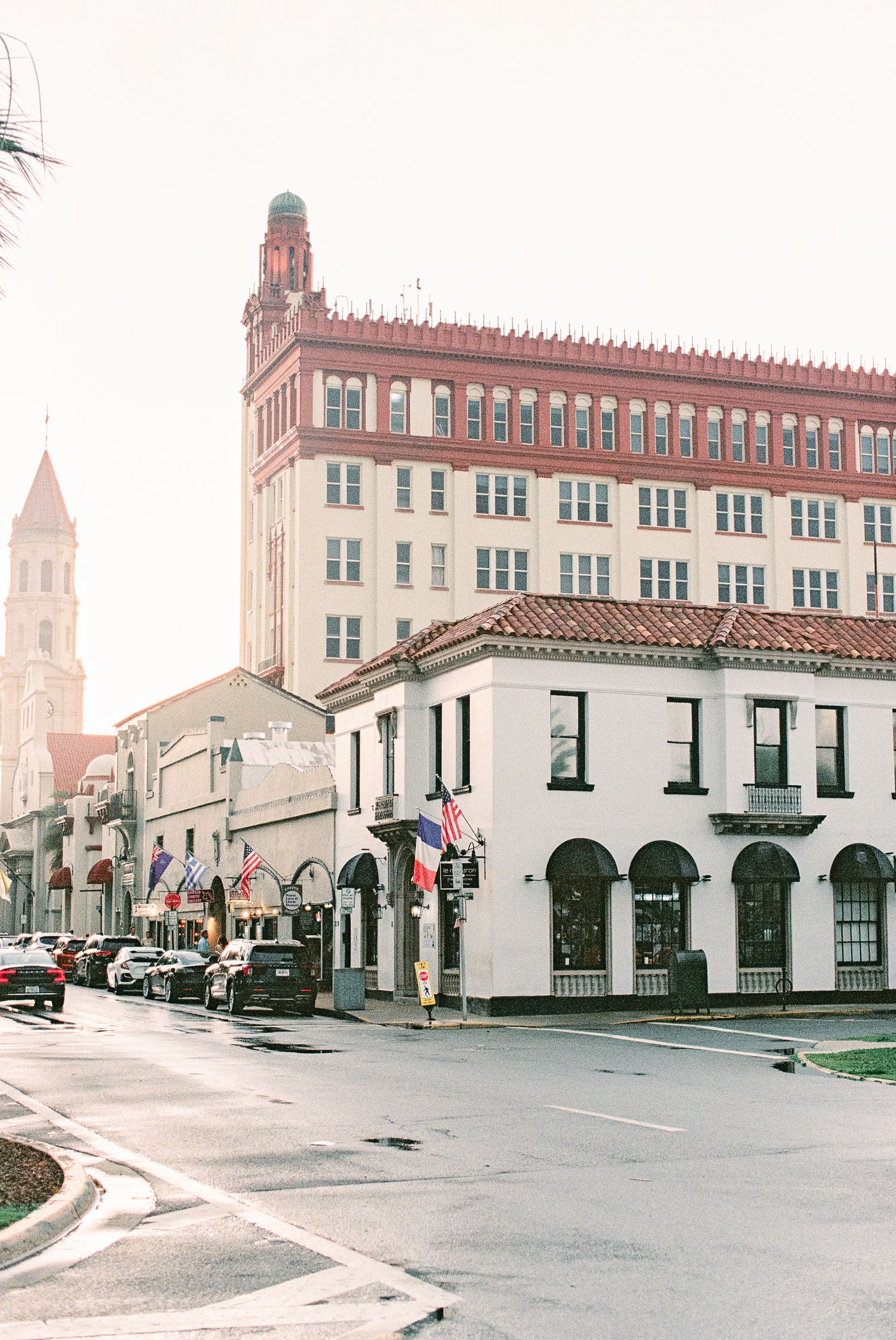 Historic downtown street corner with white Spanish Colonial building, American flags, and red-brick tower in St. Augustine, FL.