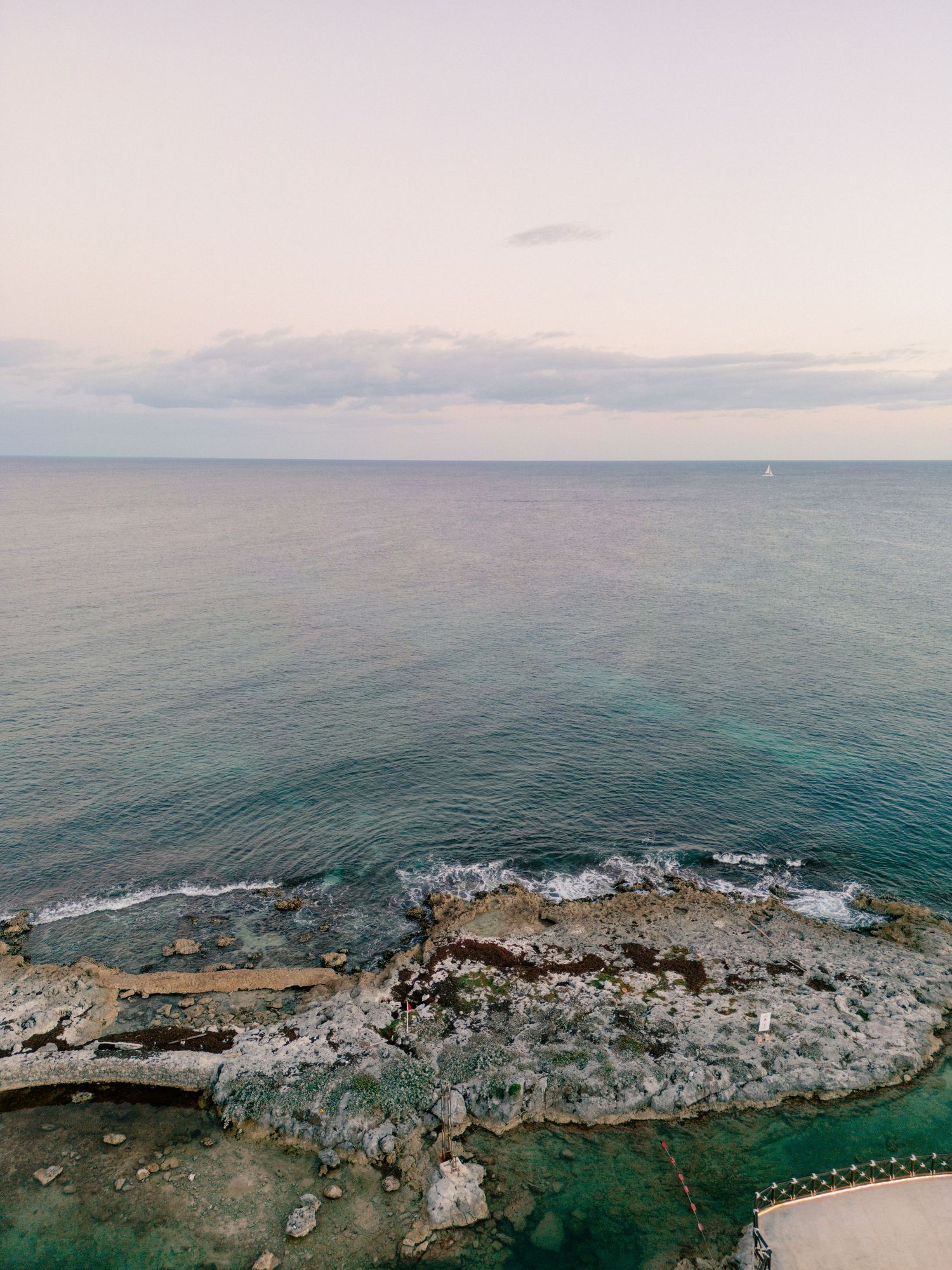 Aerial view of rocky coastline meeting turquoise Caribbean sea waters at dusk with calm horizon.