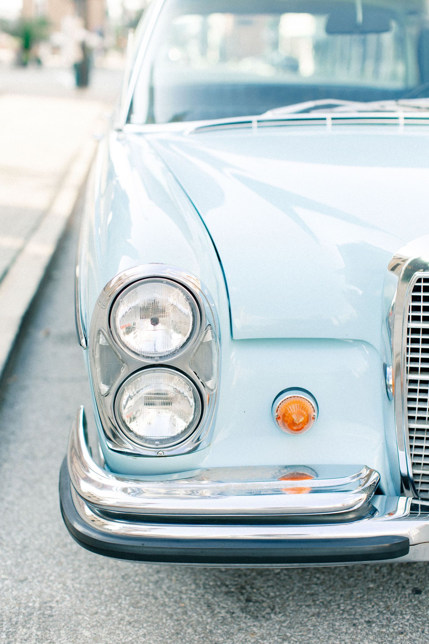 Front view of a vintage light blue classic car with chrome bumper and round headlights parked on a street.
