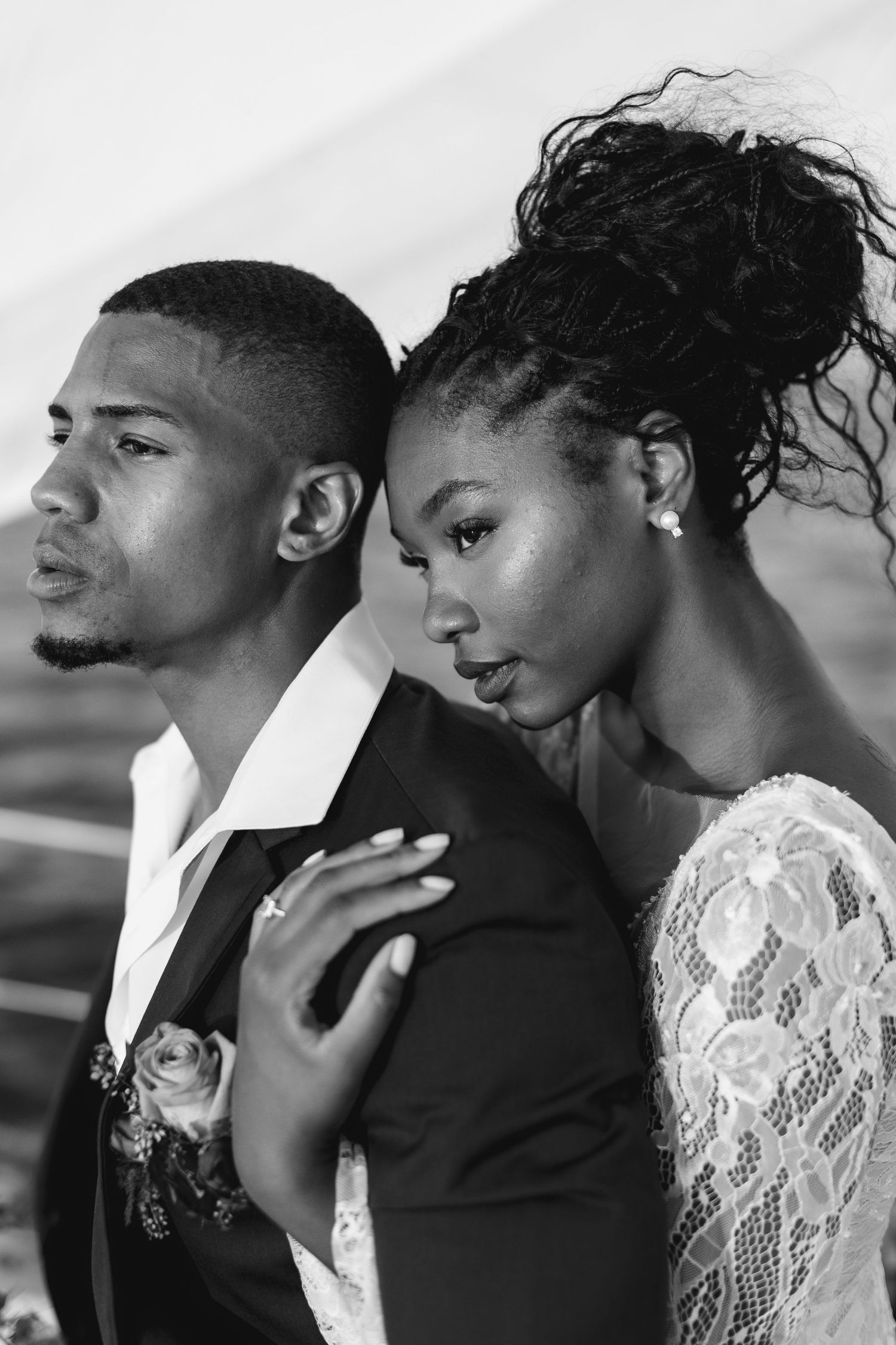 Black and white photo of a bride leaning on groom's shoulder in wedding attire.