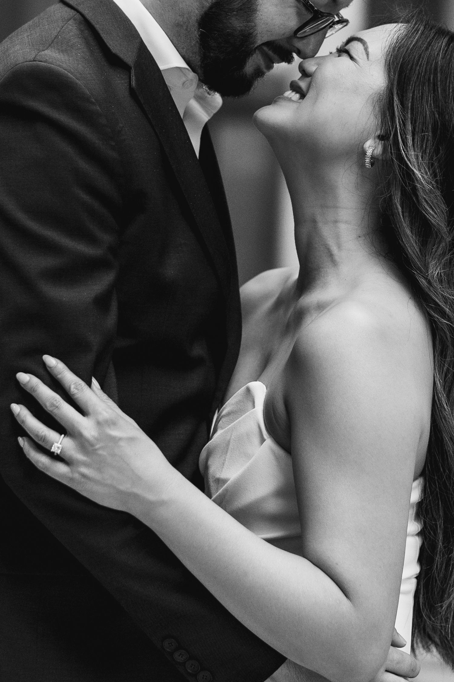 Black and white photo of a bride and groom sharing a romantic moment, with her ring visible as they embrace.