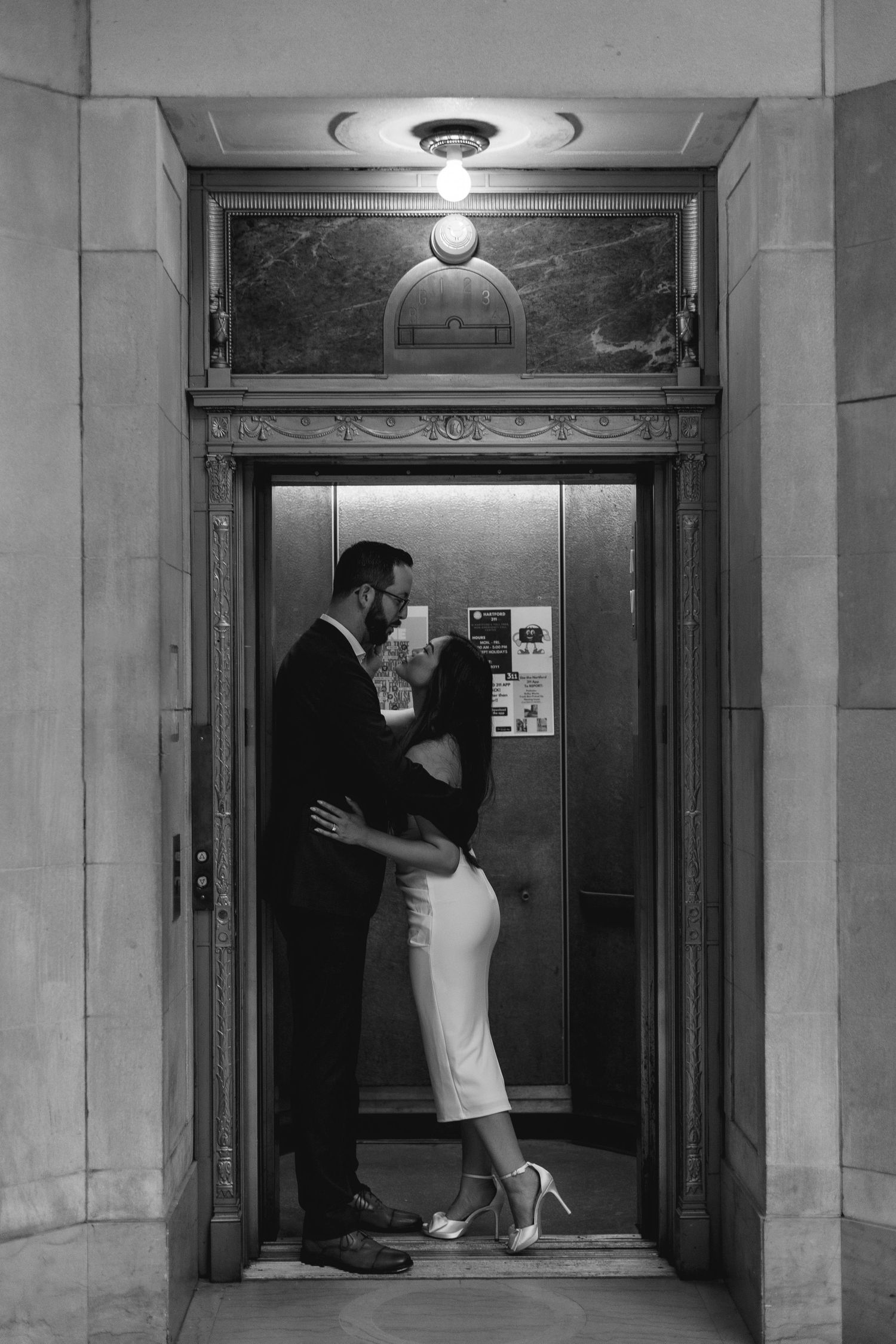 Couple sharing a romantic kiss inside an ornate vintage elevator in black and white photography.