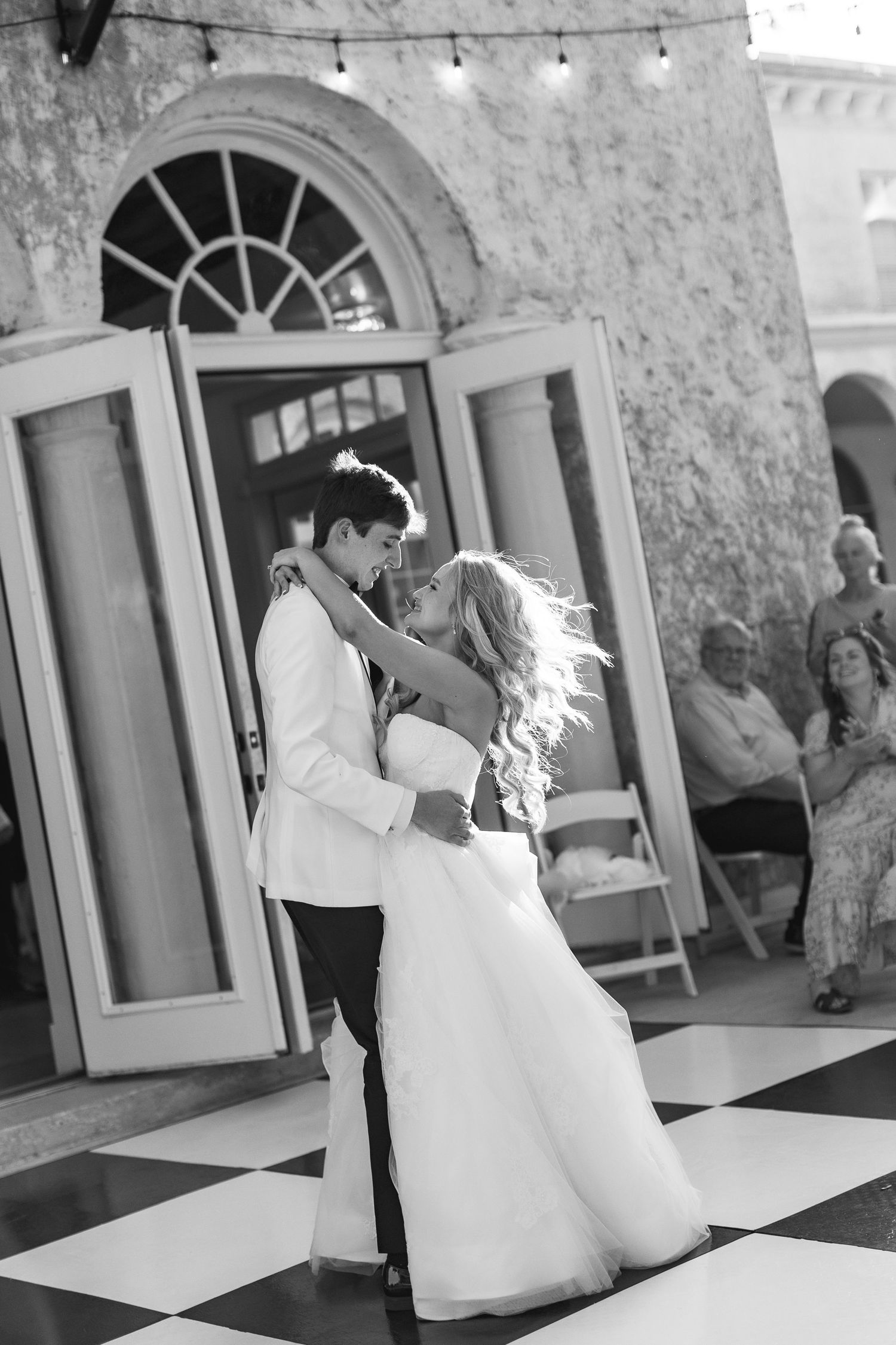 Black and white photo of bride and groom sharing first dance on checkered floor at elegant outdoor wedding reception, wedding at Bella Cosa