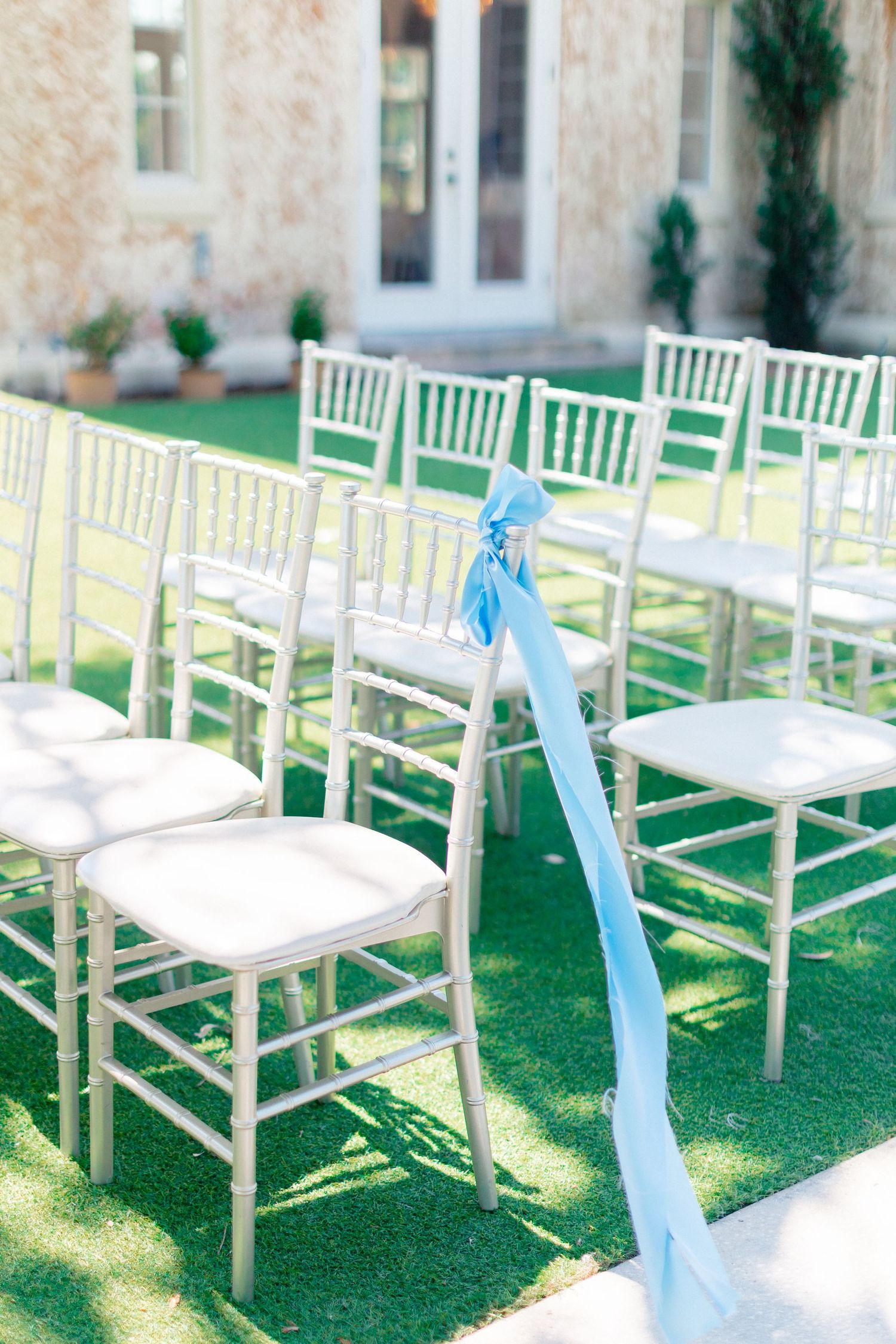 White Chiavari chairs with light blue ribbon decor arranged on green grass for an elegant outdoor wedding ceremony, wedding at Bella Cosa