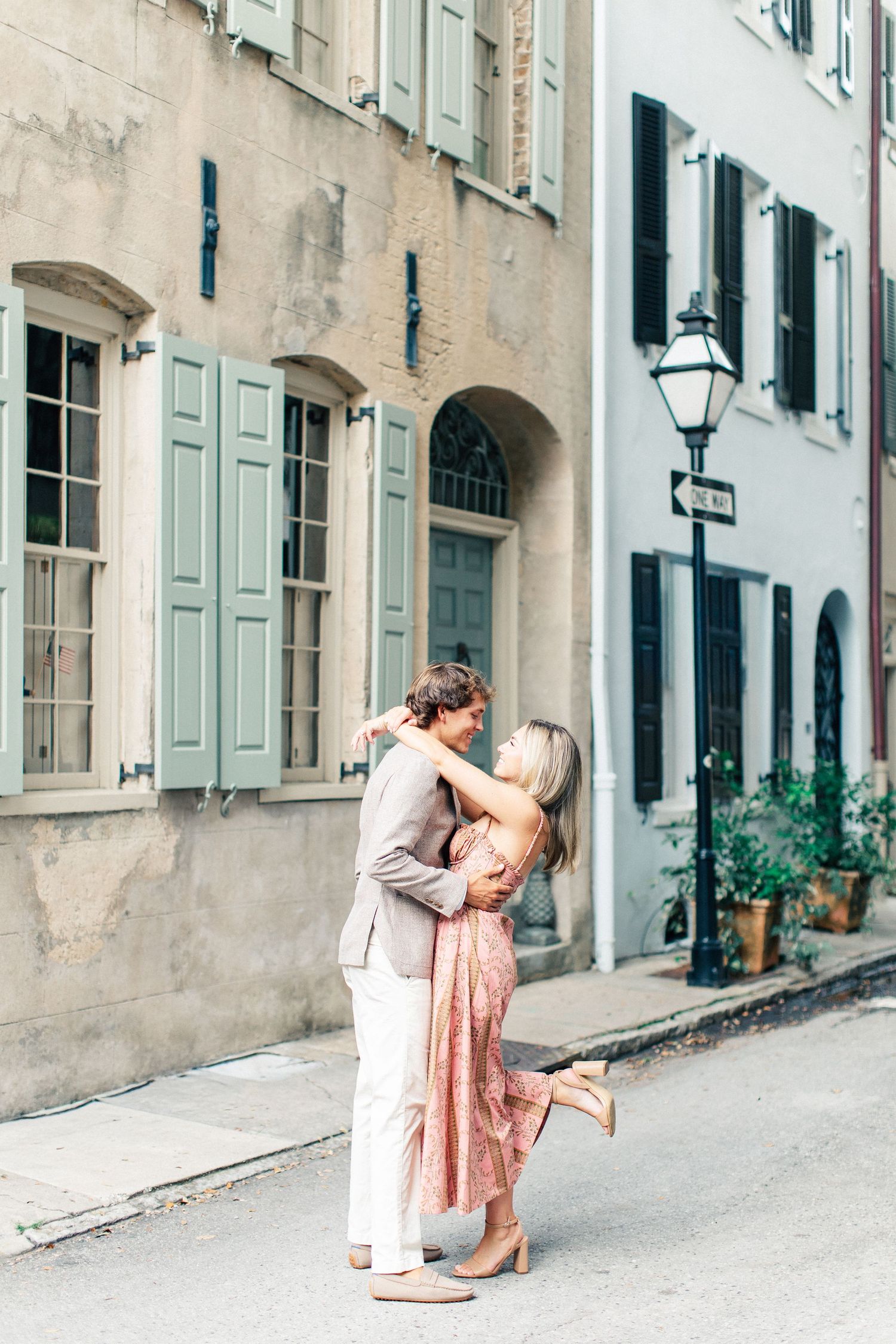 Couple embracing and dancing on a charming cobblestone street lined with pastel buildings and shutters.