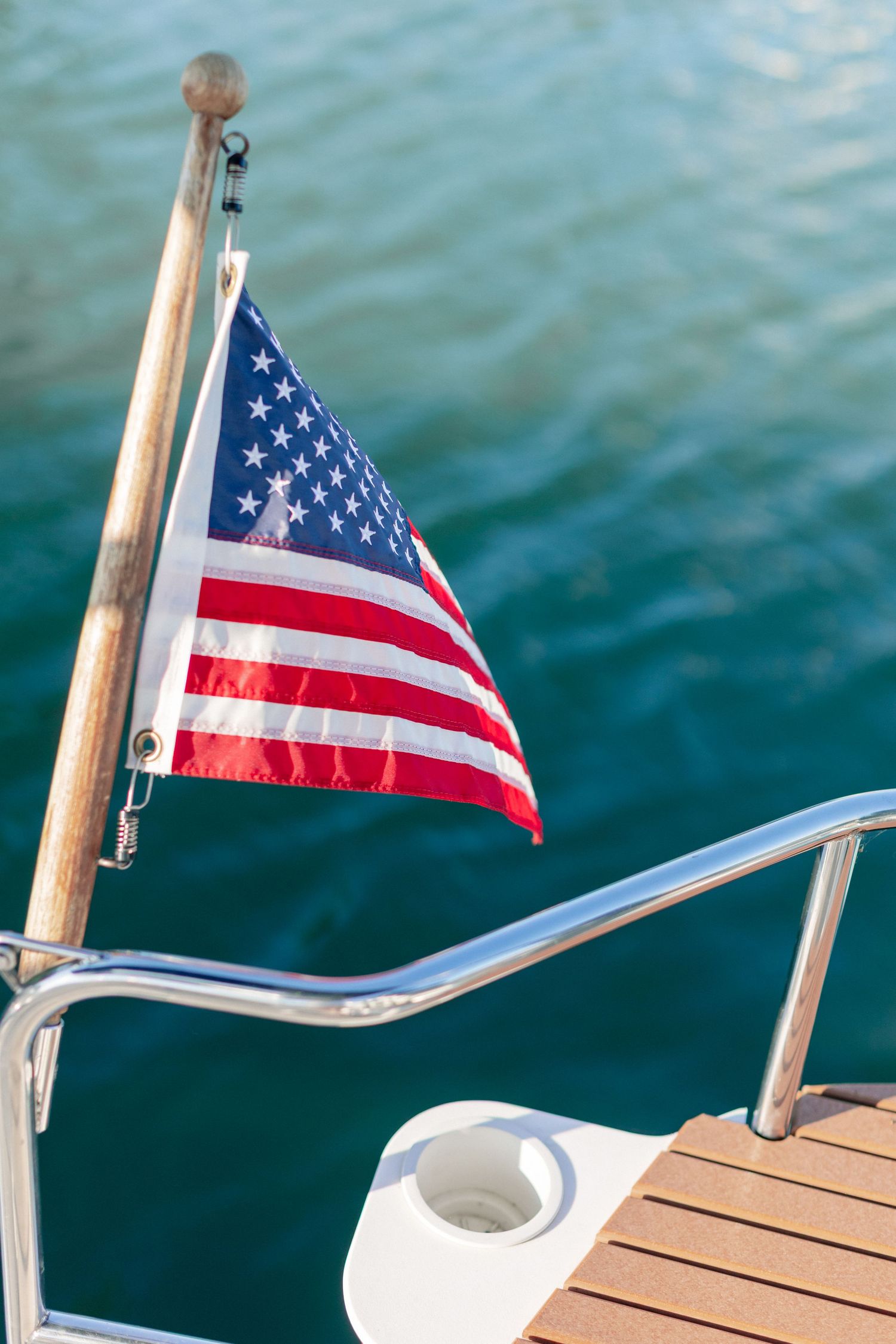 American flag waving on the stern of a yacht with turquoise water in the background on a sunny day.