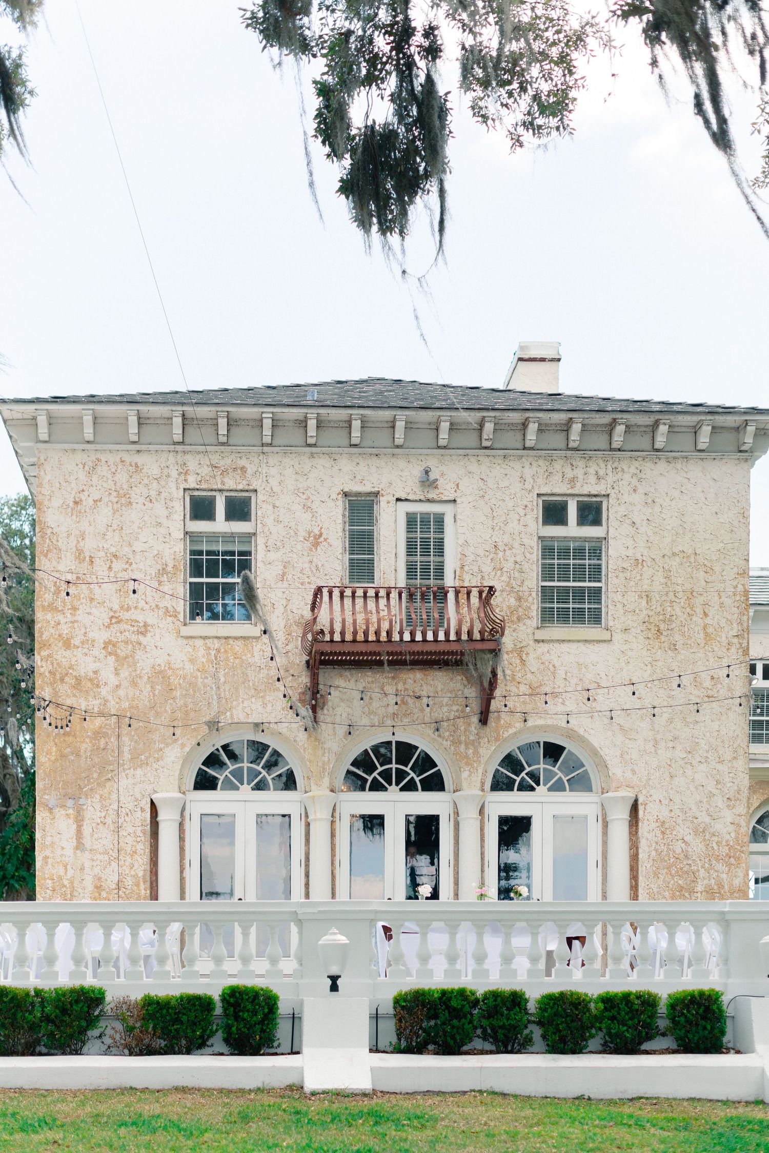 Historic two-story Southern mansion with arched windows, white balustrade fence, and Spanish moss-draped trees in soft natural light Florida