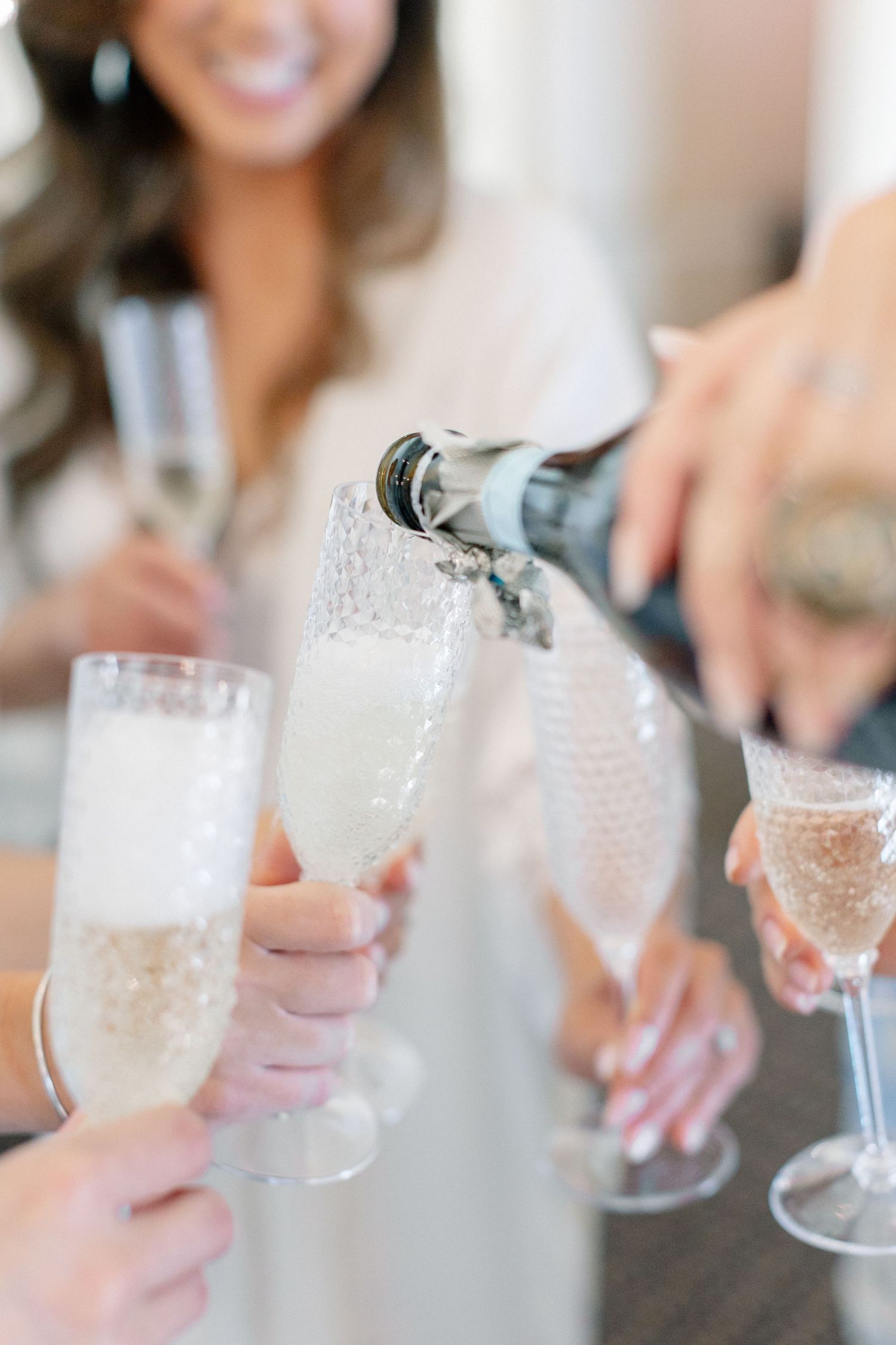 Champagne being poured into elegant flutes at a wedding celebration with bridesmaids toasting in white.