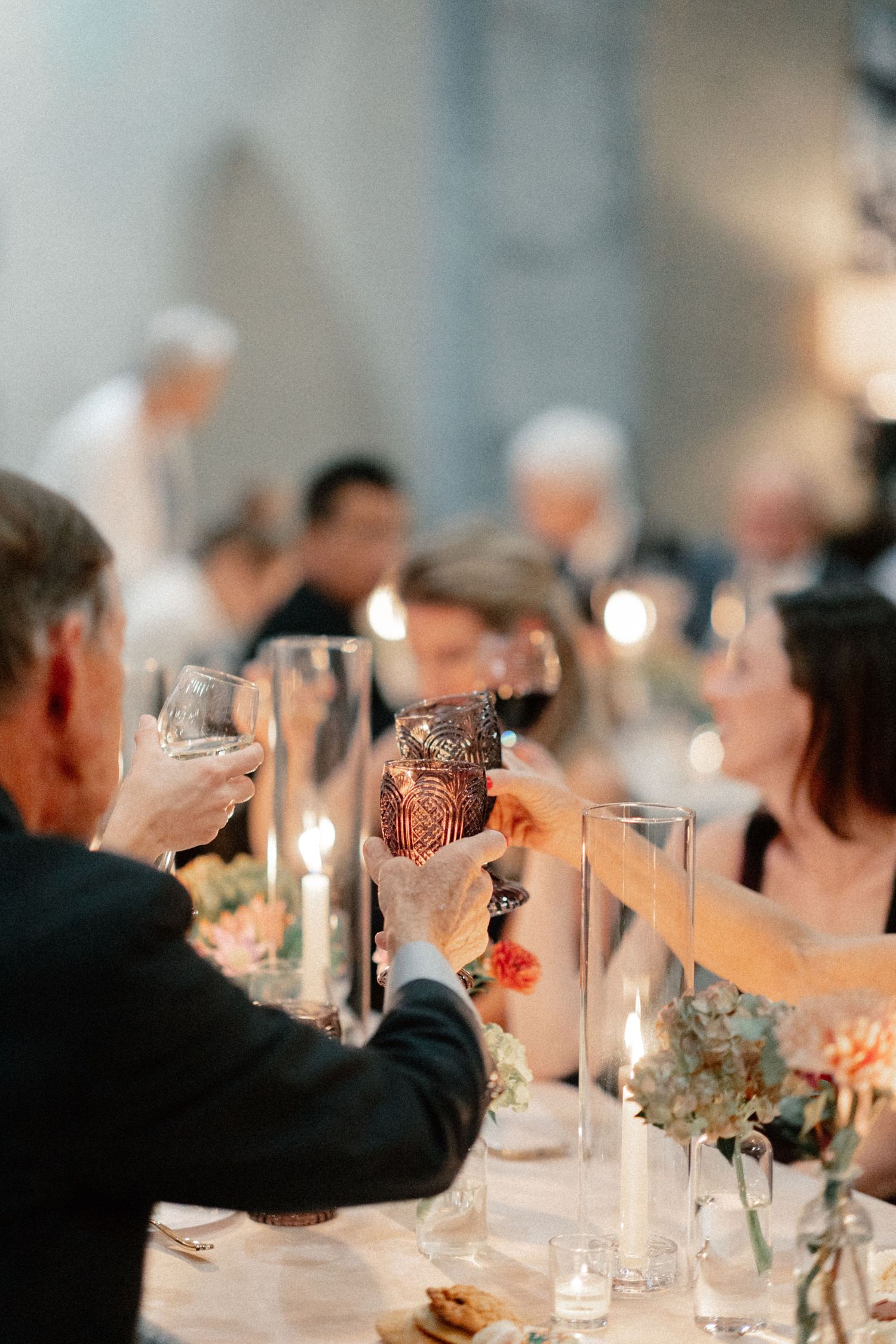 Wedding guests raising glasses in a toast at a candlelit reception dinner.