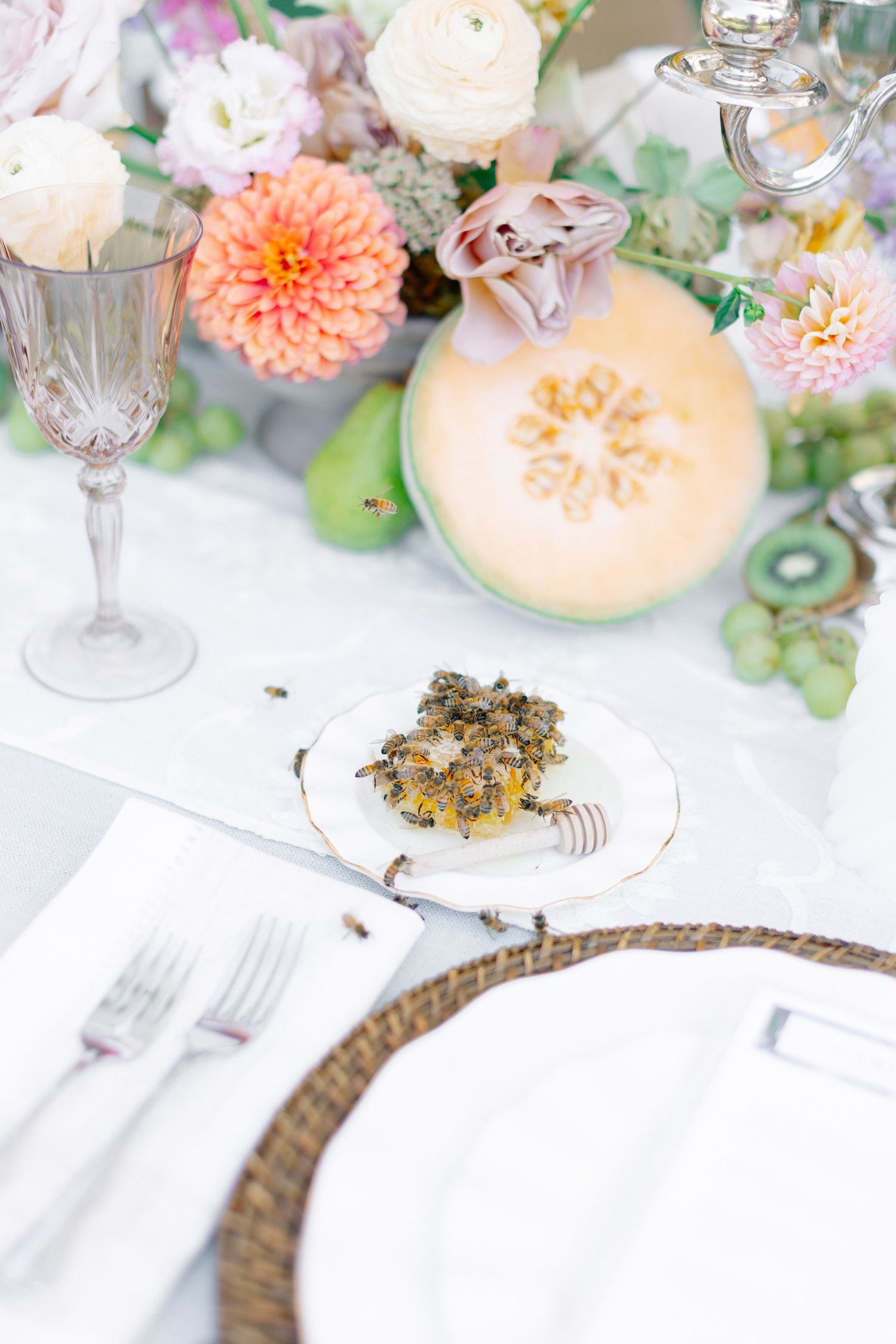 Close-up of wedding table detail with oyster appetizer, crystal glassware, fresh melon, and pastel floral arrangement.