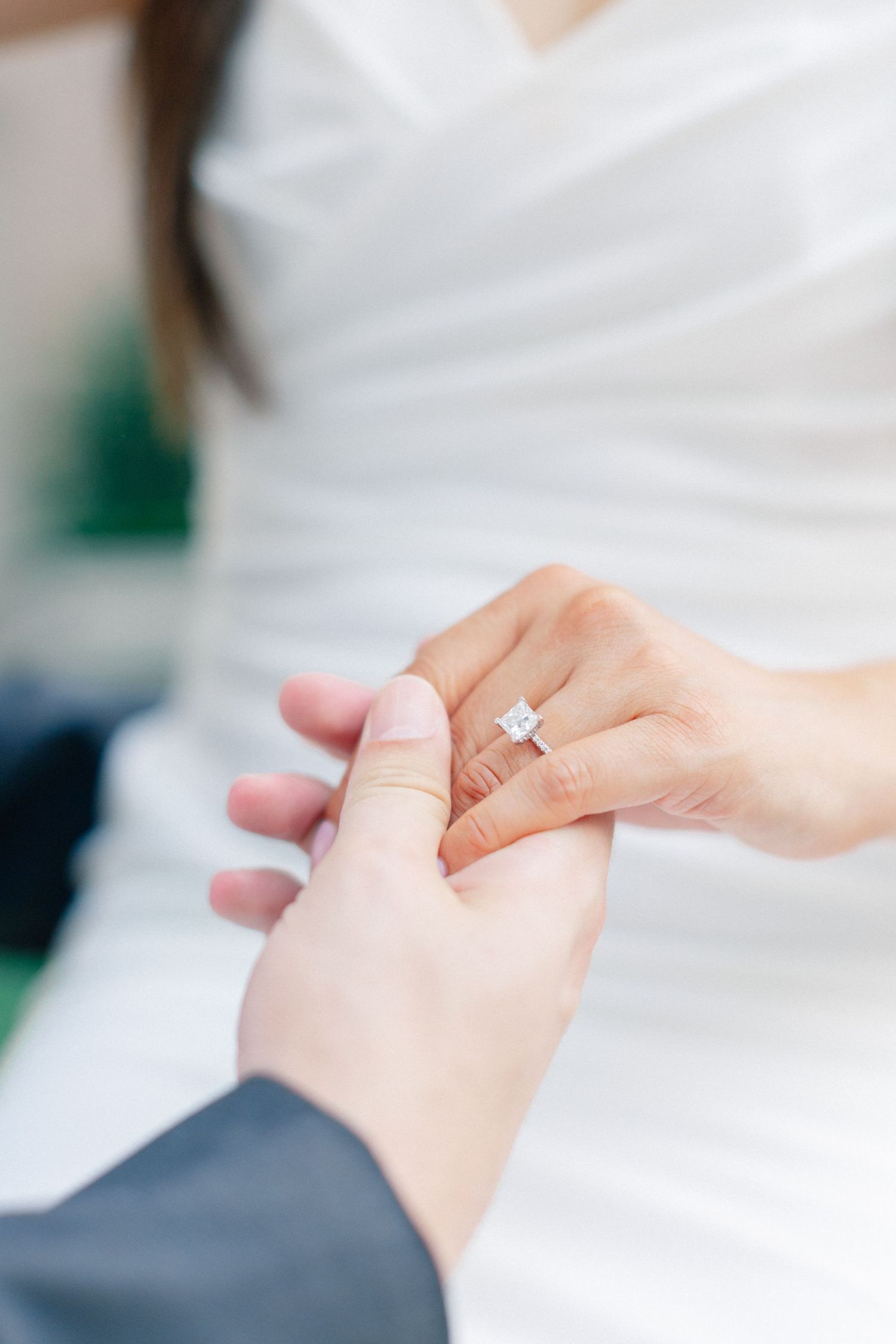Groom places a princess-cut diamond engagement ring on brides finger during wedding ceremony.