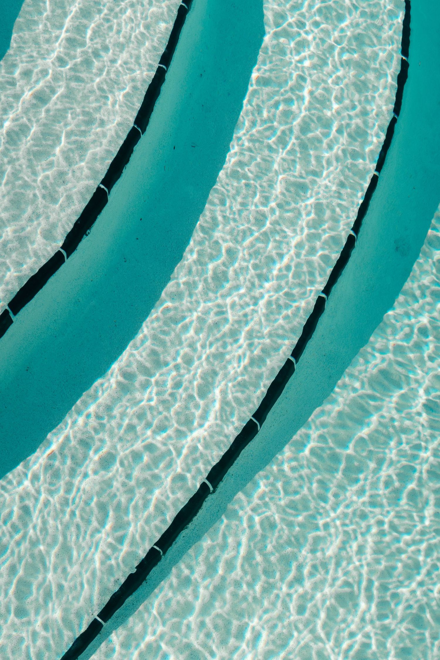 Turquoise pool steps submerged underwater with rippling light reflections creating abstract curved patterns.