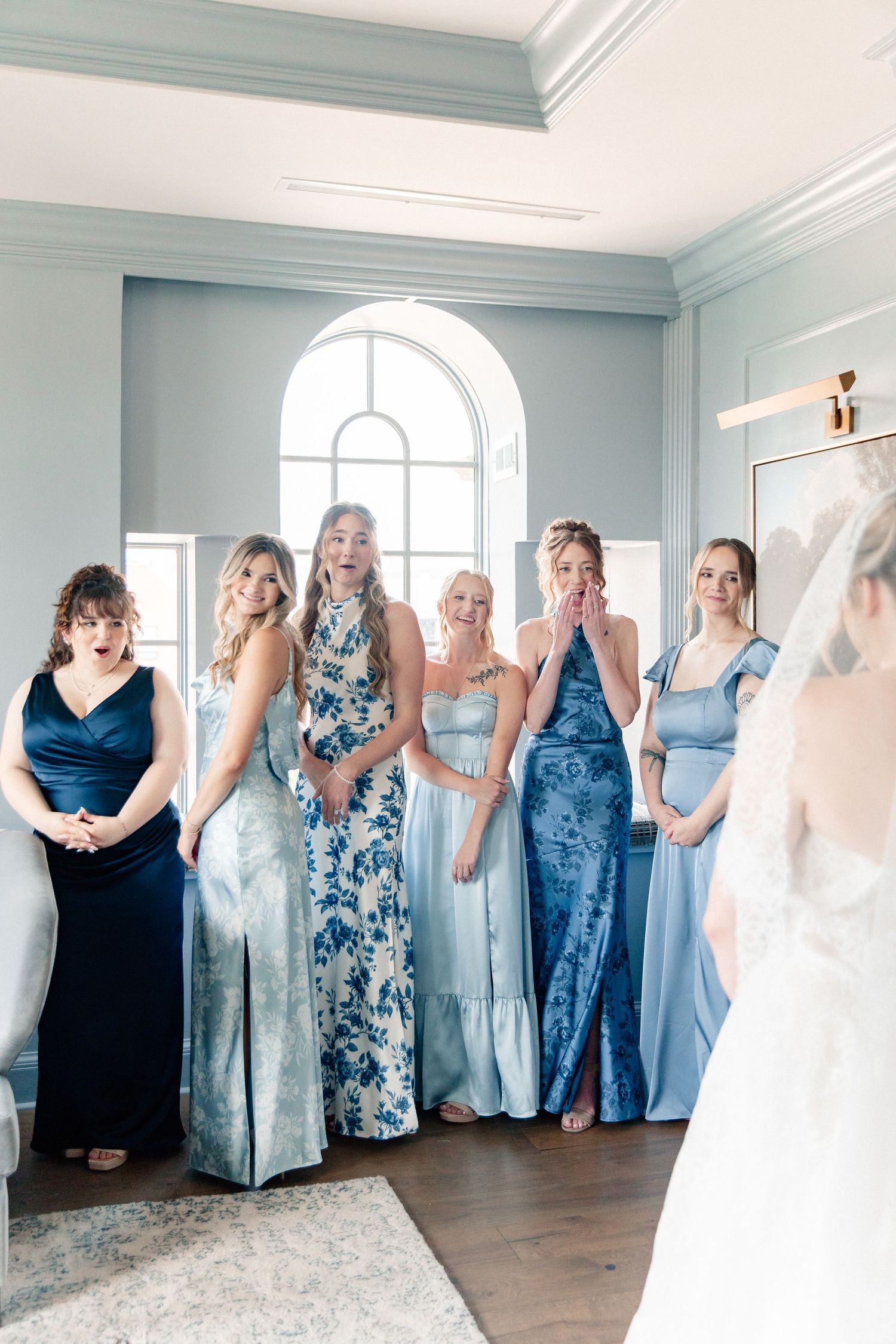 Bridesmaids in blue dresses react with joy and tears seeing the bride for the first time during a wedding morning reveal.