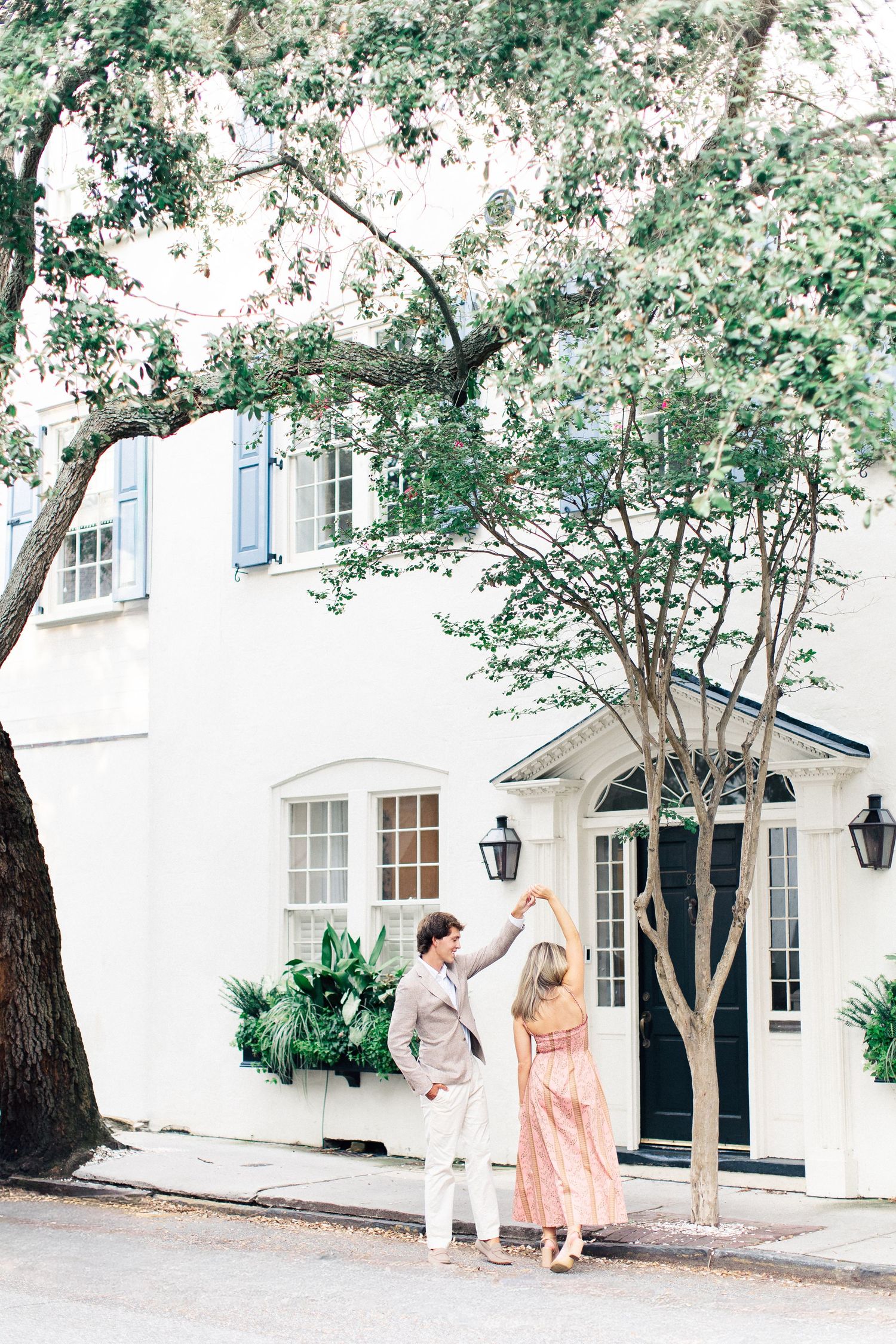 Couple dancing on a cobblestone street in front of a charming white Southern home with blue shutters.