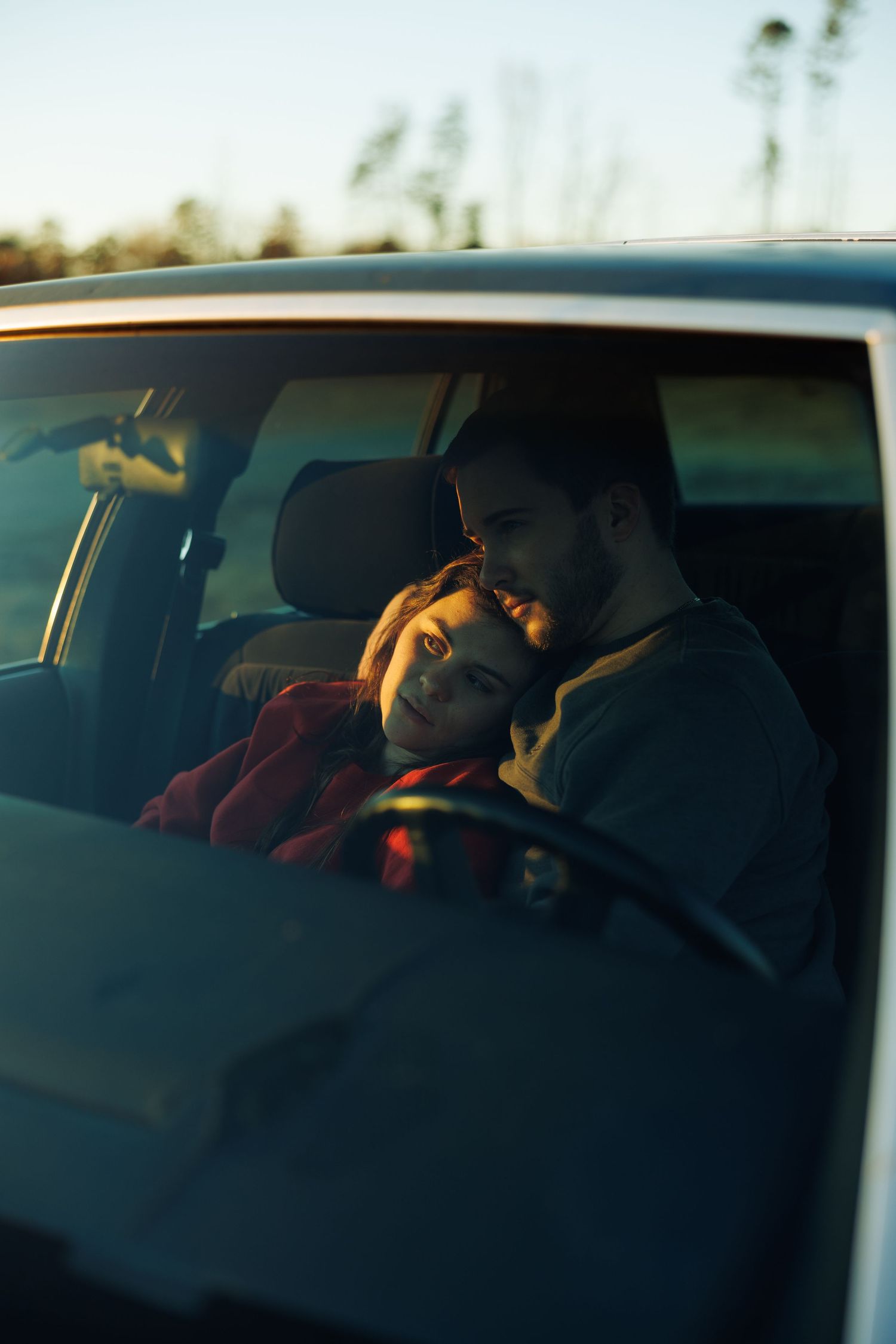 Romantic couple cuddling inside a car at sunset, woman resting head on mans shoulder.