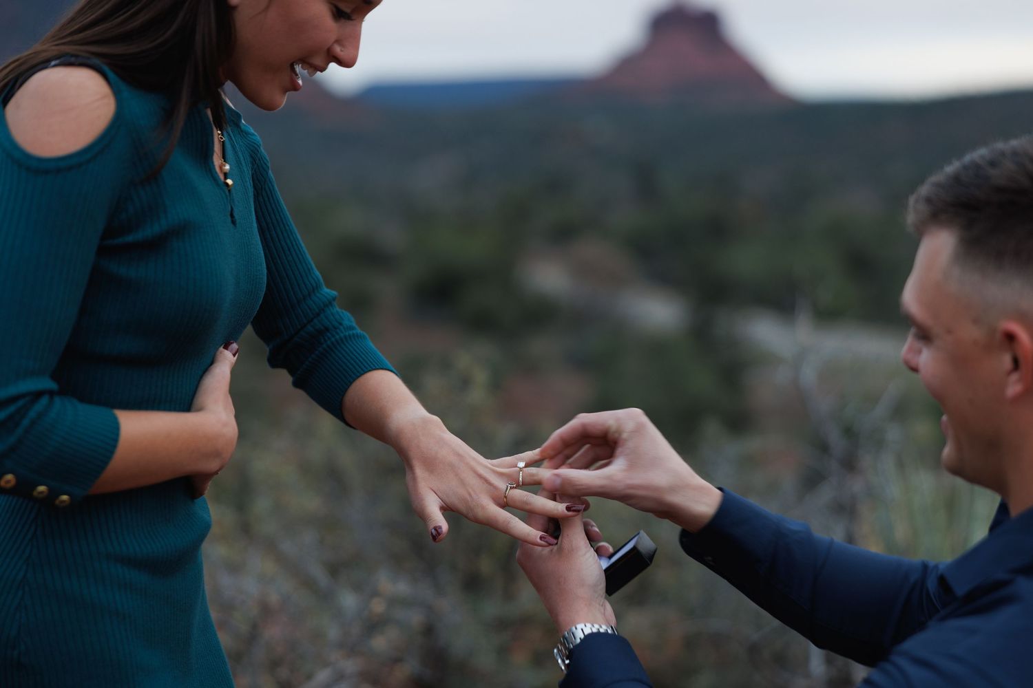 Man kneeling to propose with a ring to a woman in Sedona, Arizona, with red rock formations in the background.