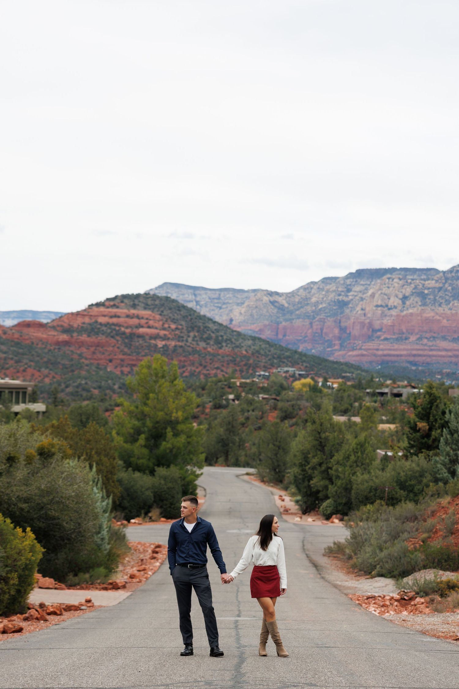 Engaged couple holding hands on empty road with stunning Sedona Arizona red rock scenery.