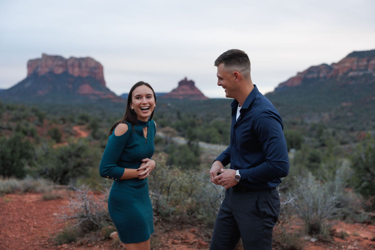 Couple laughing together at sunset in Sedona, Arizona, with iconic red rock buttes in the background.