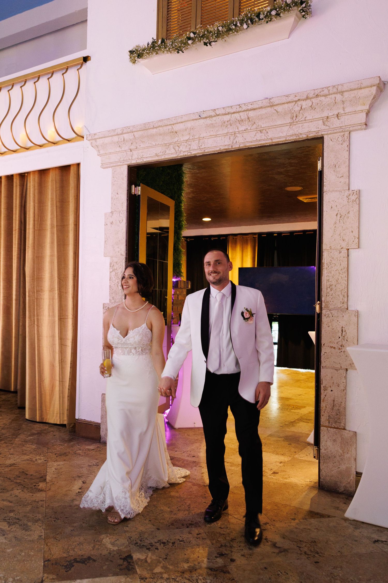 Newlyweds holding hands making grand entrance through stone archway at elegant wedding reception.