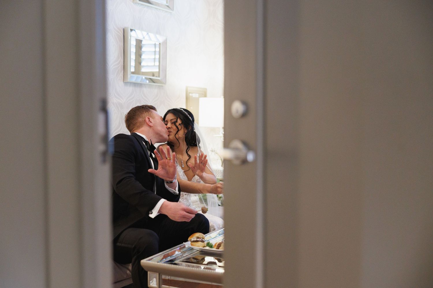 Bride and groom sharing a joyful moment together at a table, photographed through a doorway.