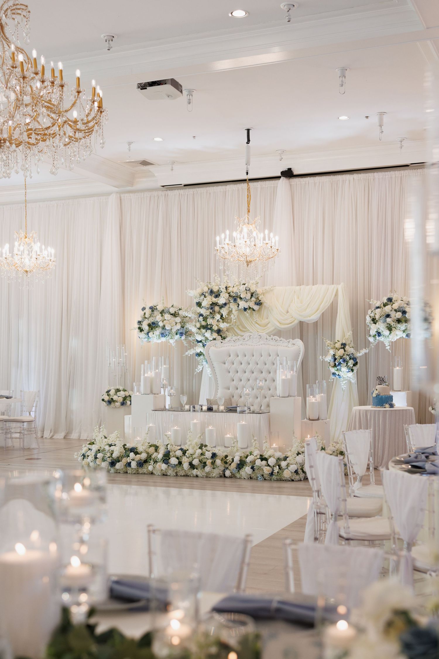 A luxurious white wedding reception ballroom with tufted sweetheart table, floral arrangements, and crystal chandeliers at The Yorkmont.