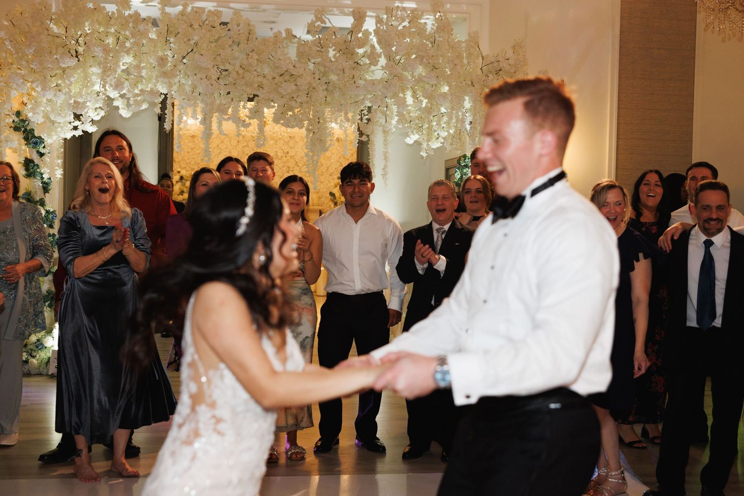 Bride in lace gown and groom in tuxedo share first dance at elegant wedding reception.