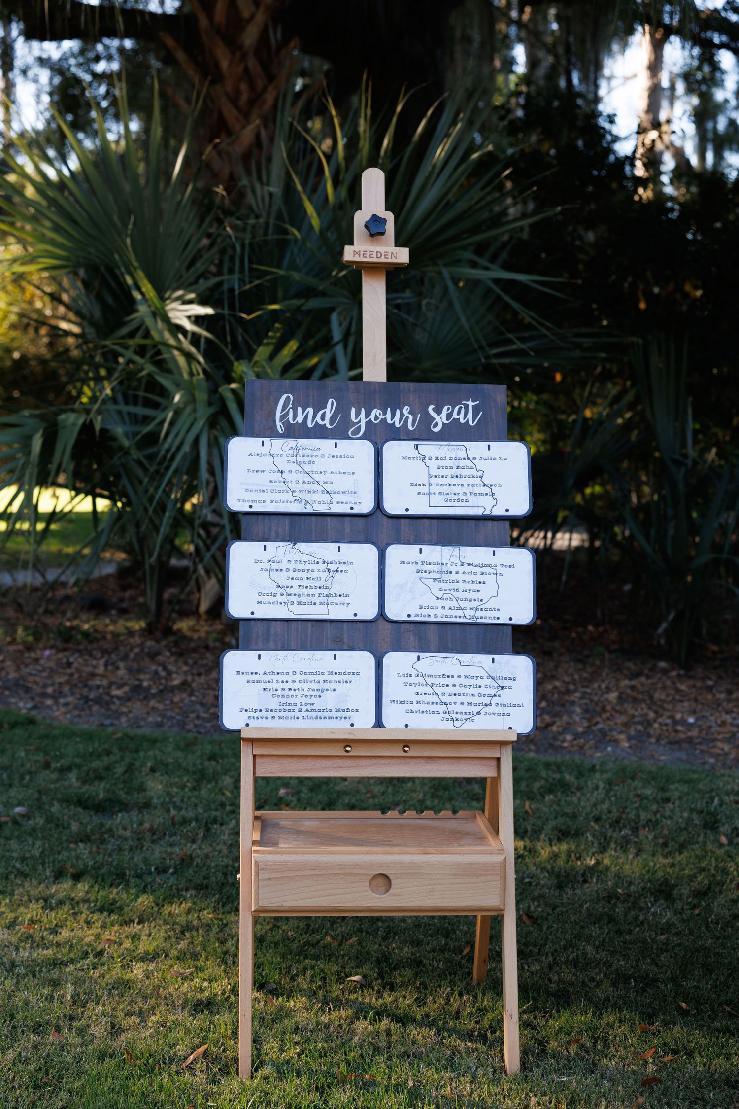 Rustic wooden easel seating chart sign reading find your seat at an outdoor wedding venue.