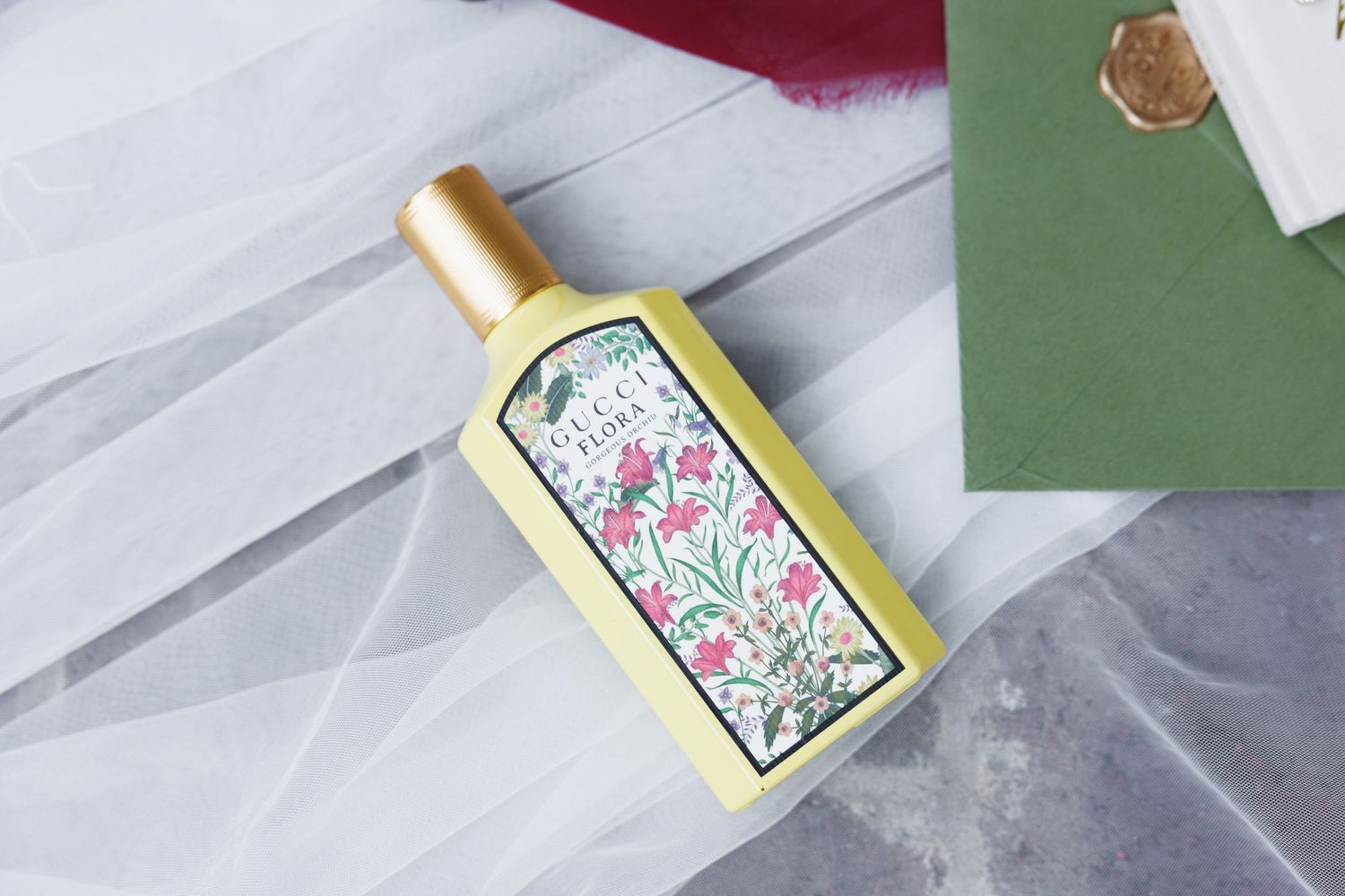 Gucci Flora perfume bottle with floral design and gold cap on white fabric background.