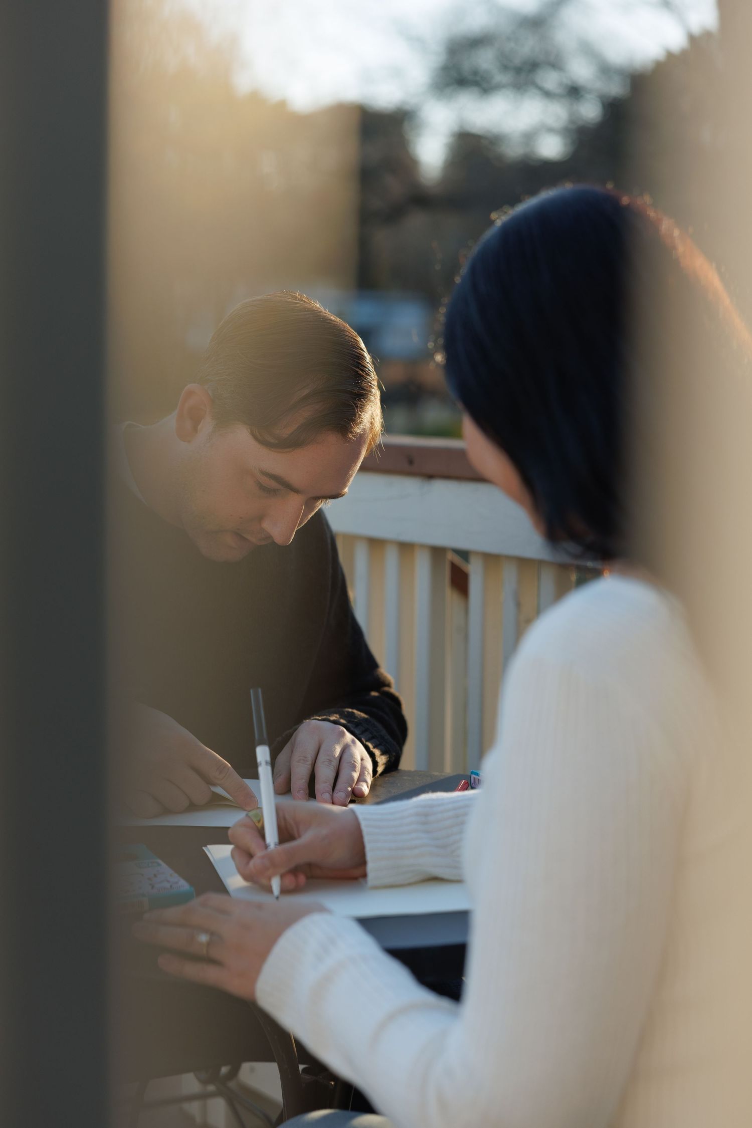 Couple sitting outdoors at a table writing notes together in warm golden sunset light.