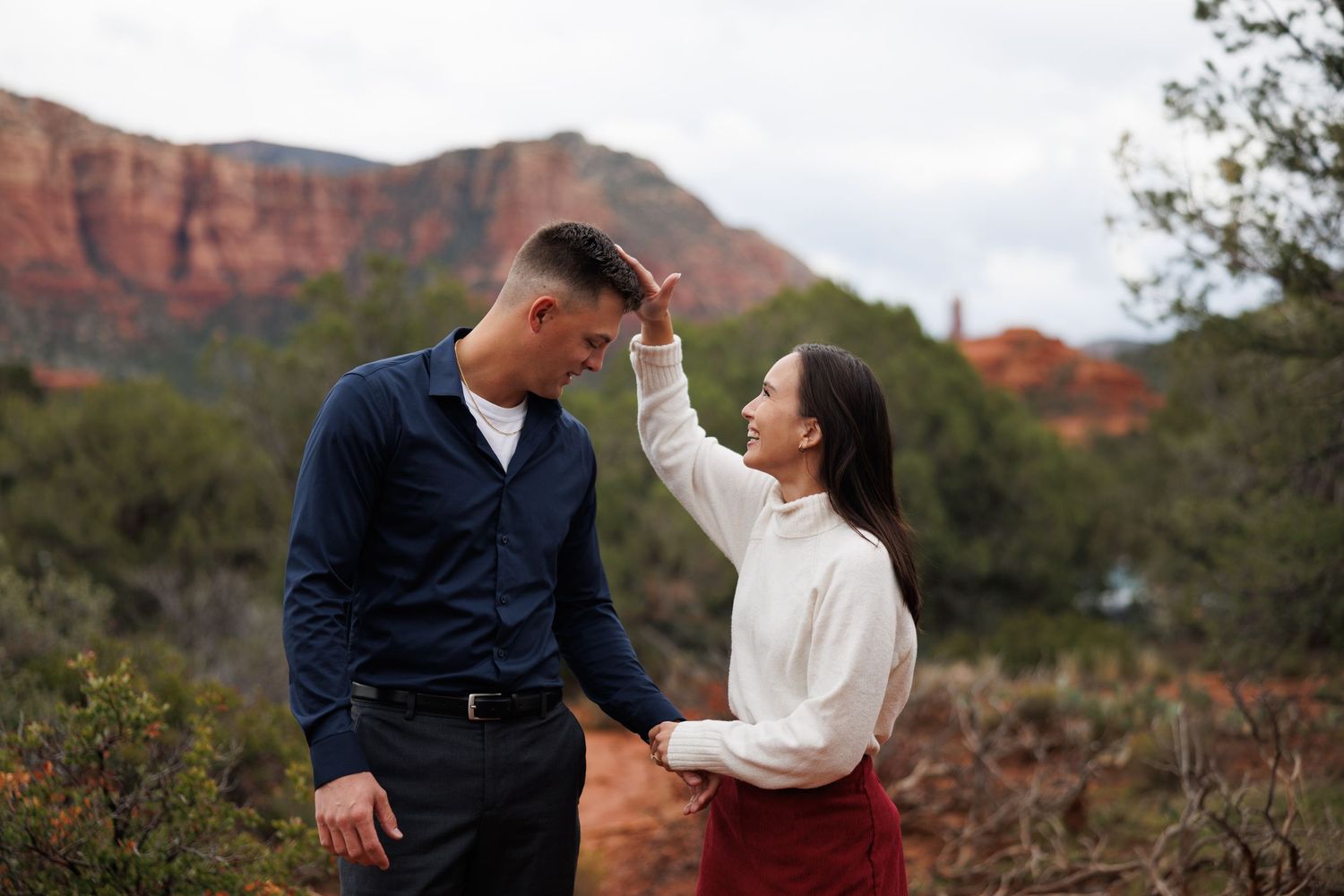 Couple sharing a playful moment with red rock formations in the background during a Sedona engagement session.