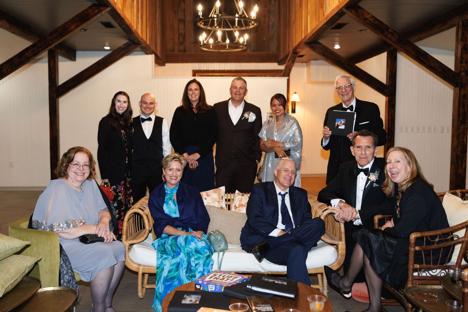 Wedding guests and family posing together inside rustic barn reception venue with chandelier lighting.