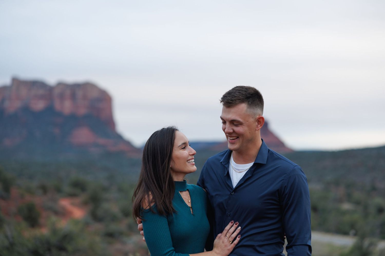 Couple embracing and smiling at each other with Sedona red rock butte backdrop.