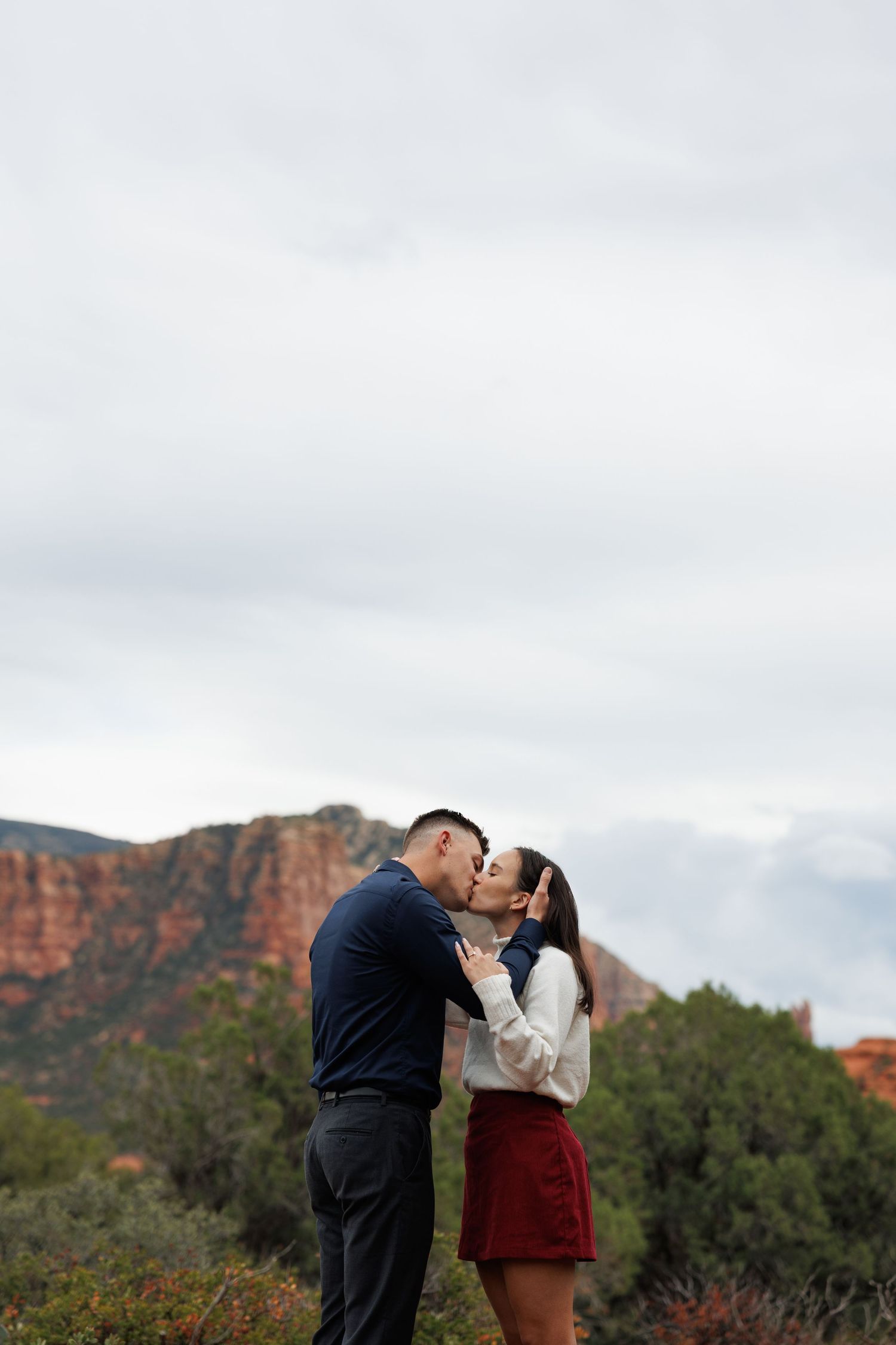 Couple sharing a romantic kiss with Sedona Arizona red rock canyon landscape behind them.
