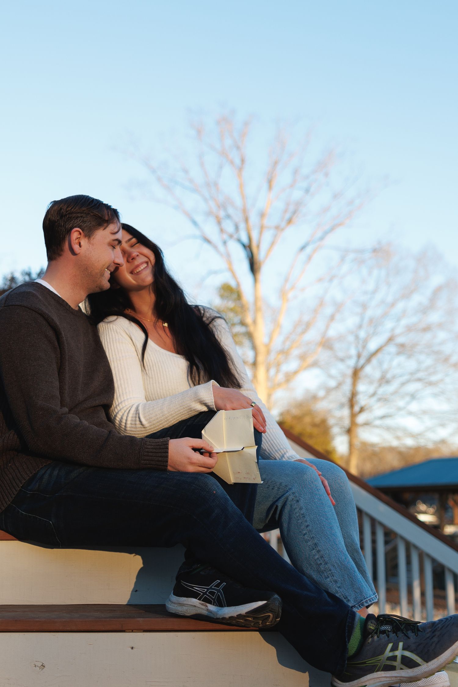 Couple sitting together on outdoor steps at sunset, sharing a tender moment with a gift box.