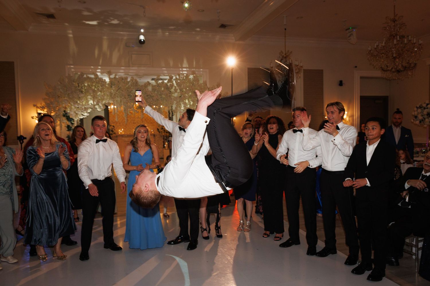 Groom performs dramatic backflip on dance floor surrounded by cheering wedding guests during reception at The Yorkmont in Charlotte, North C