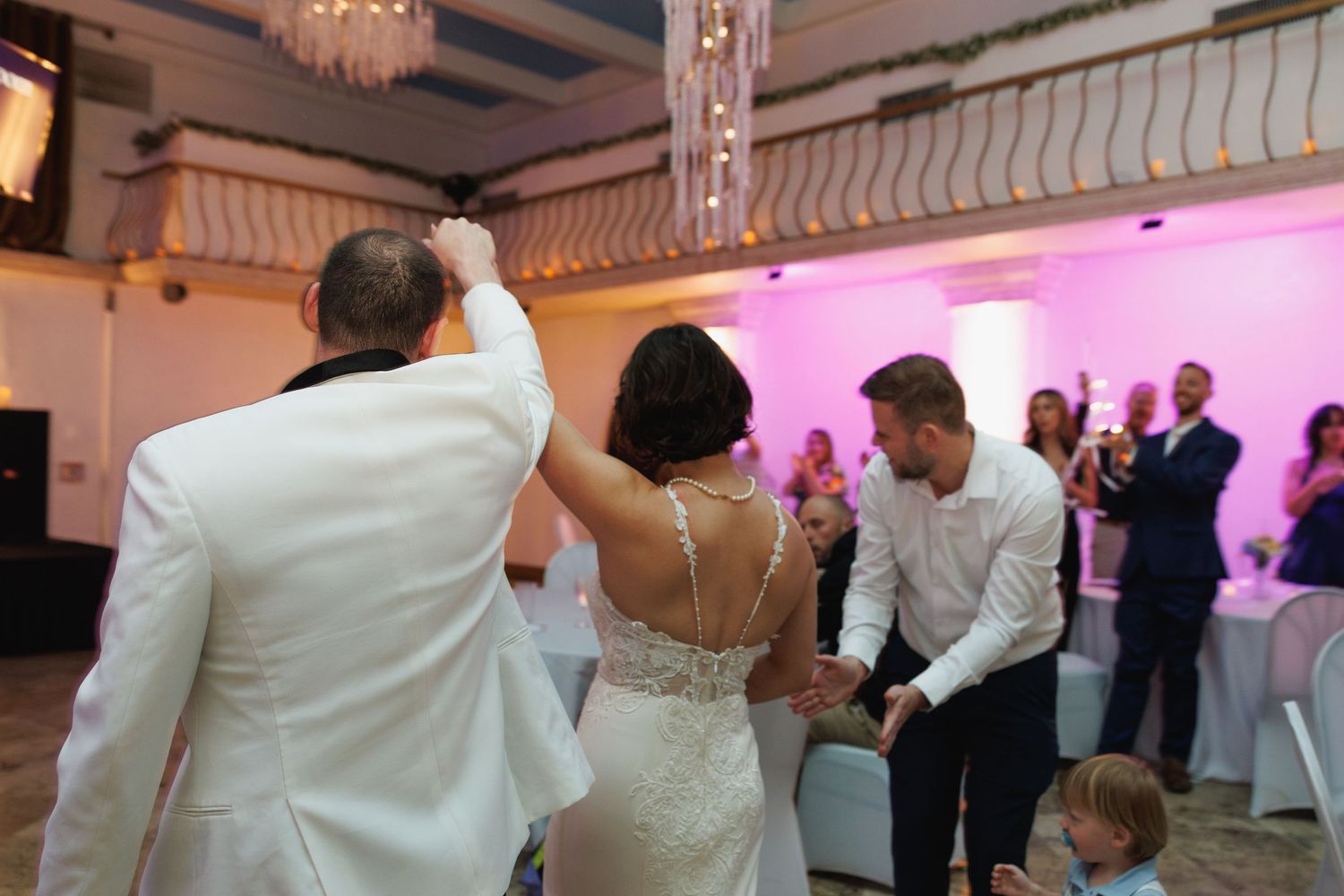 Bride and groom sharing first dance at elegant wedding reception with pink lighting.