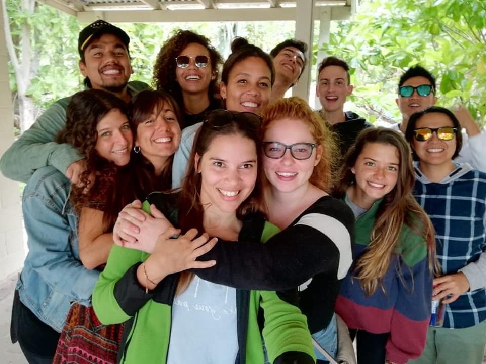 A diverse group of smiling young people posing together for a cheerful group selfie outdoors.
