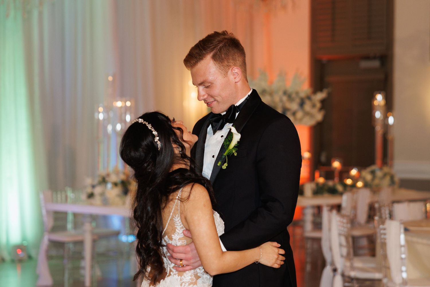Bride and groom share romantic first dance embrace in softly lit elegant wedding reception venue.