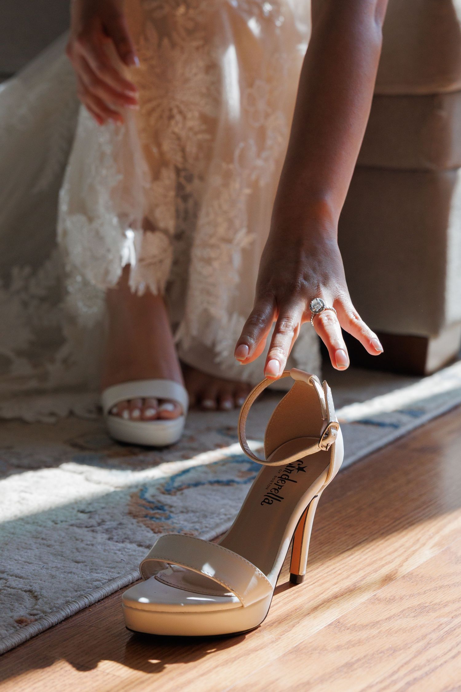 Bride putting on white platform heels while wearing lace wedding dress with diamond ring.