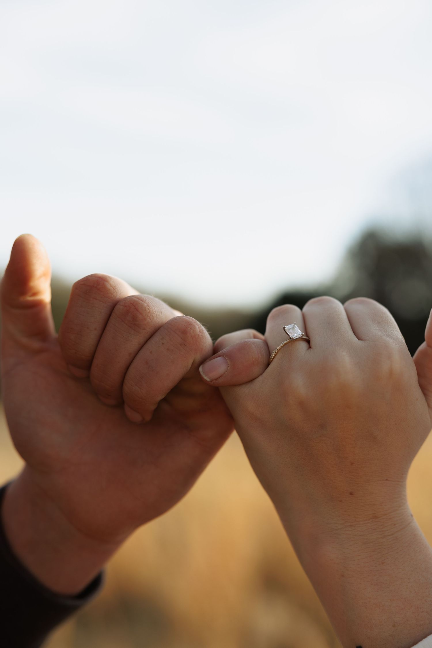 Close-up of couple doing a pinky promise with an engagement ring on the woman's hand.