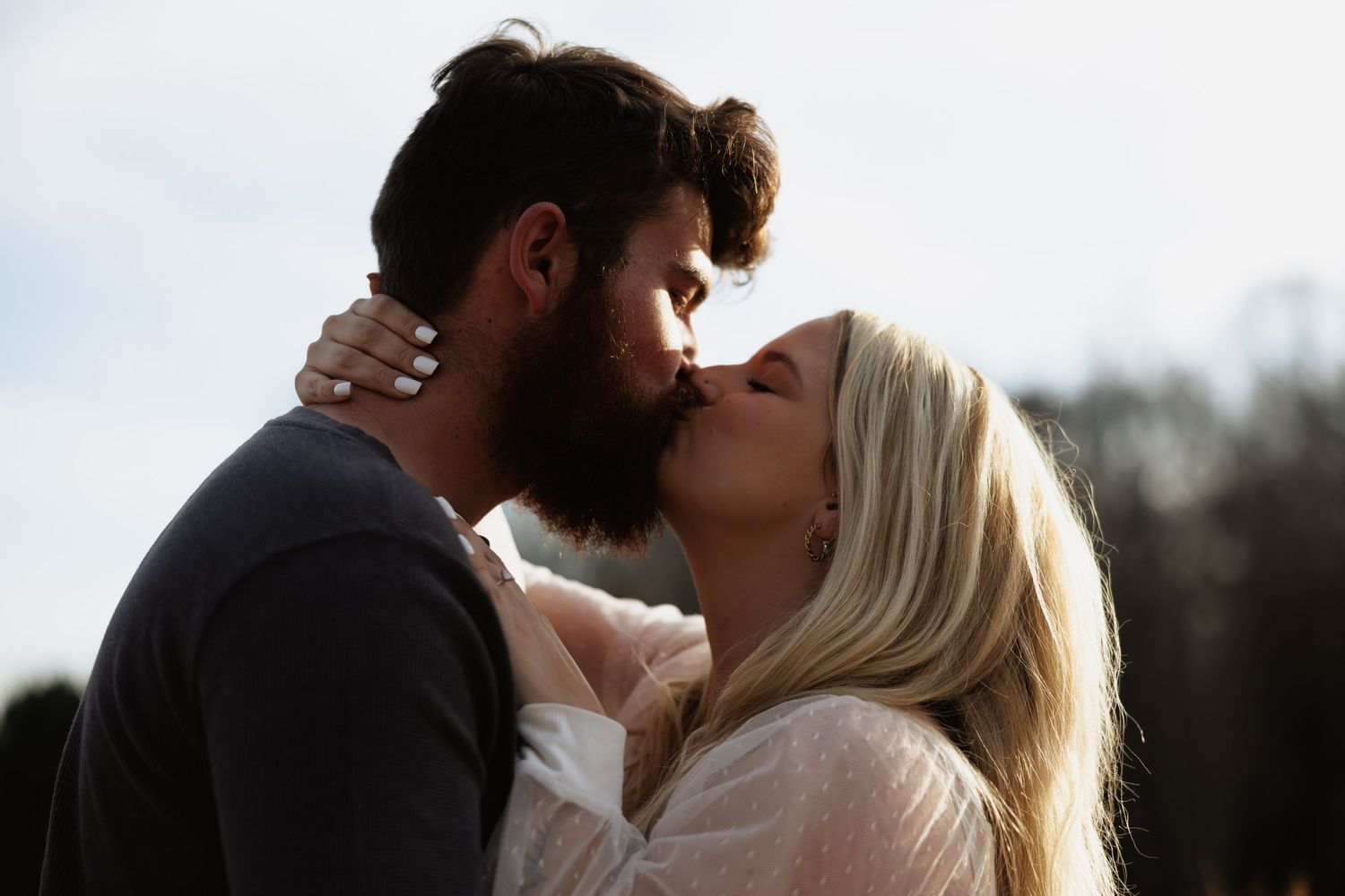 Couple sharing a romantic kiss outdoors with soft natural light in the background.