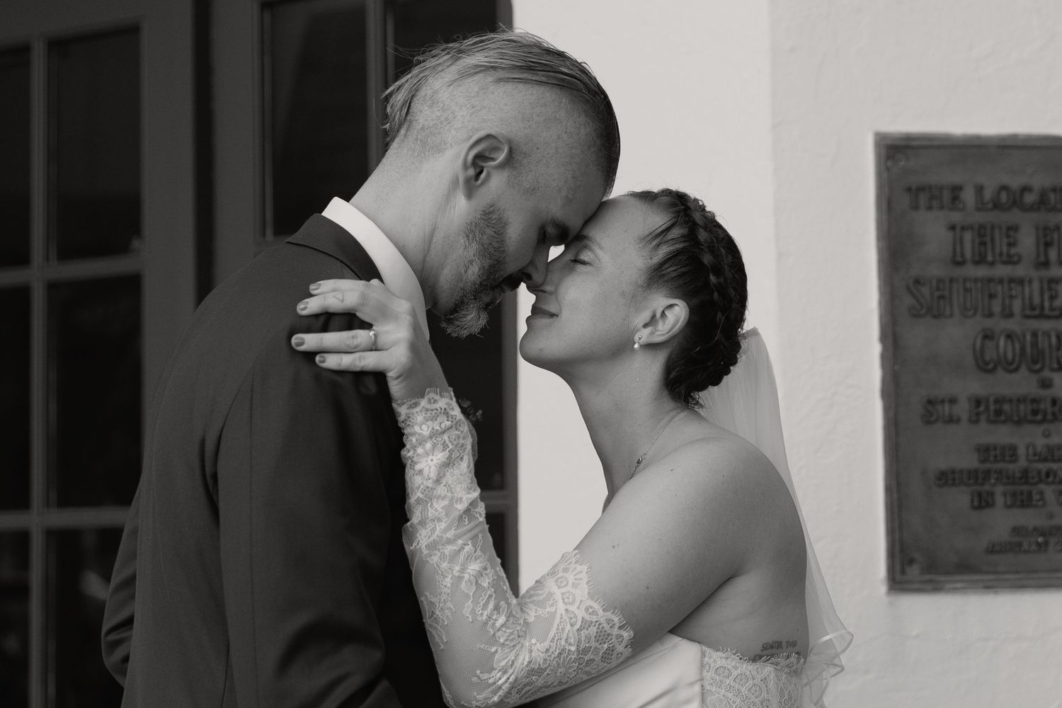 A black and white photo of a bride and groom touching foreheads romantically outside a historic building.