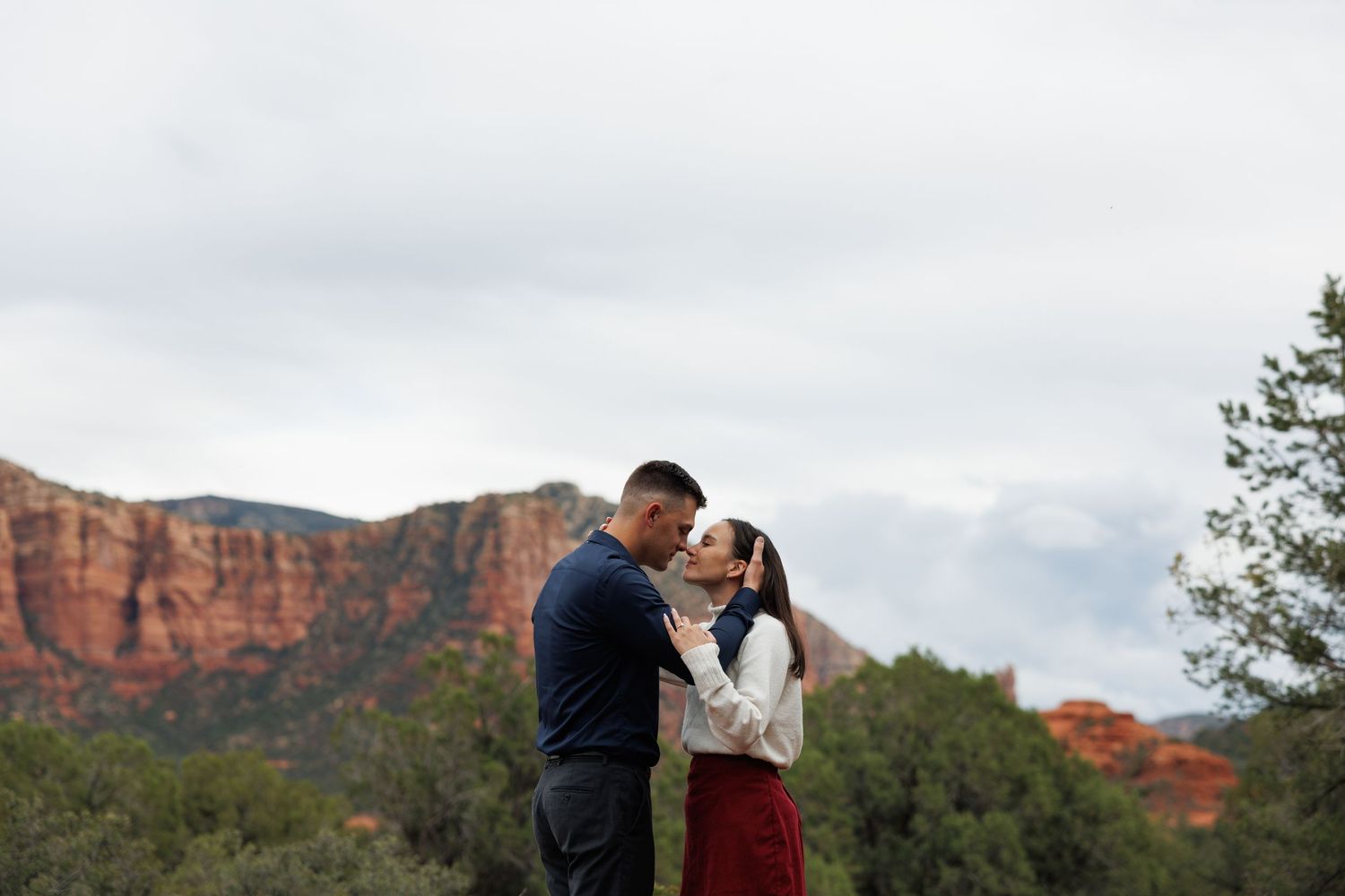Romantic couple sharing a kiss surrounded by Sedona red rock scenery.