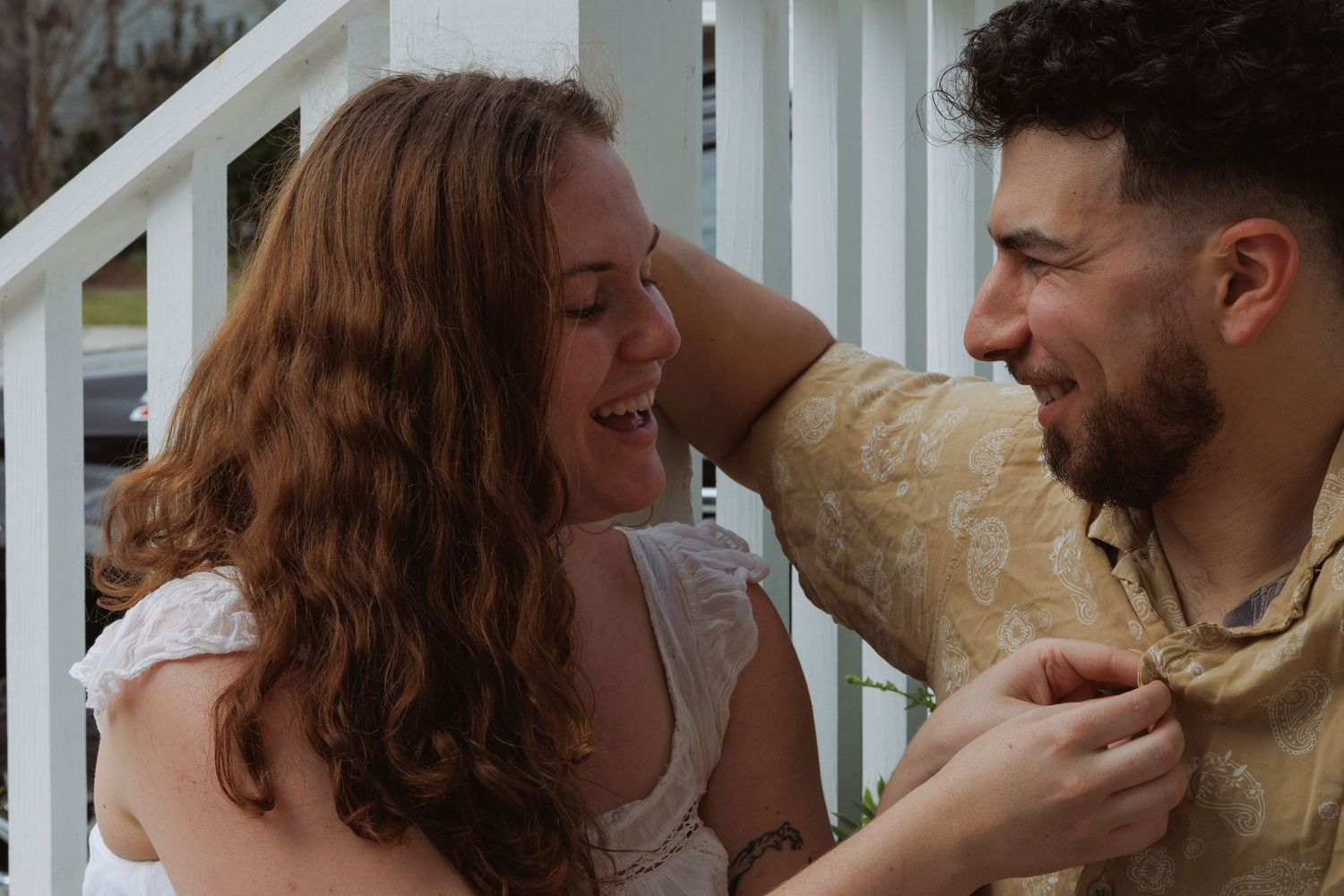 A young couple laughing and smiling together on a porch, sharing a joyful moment outdoors.