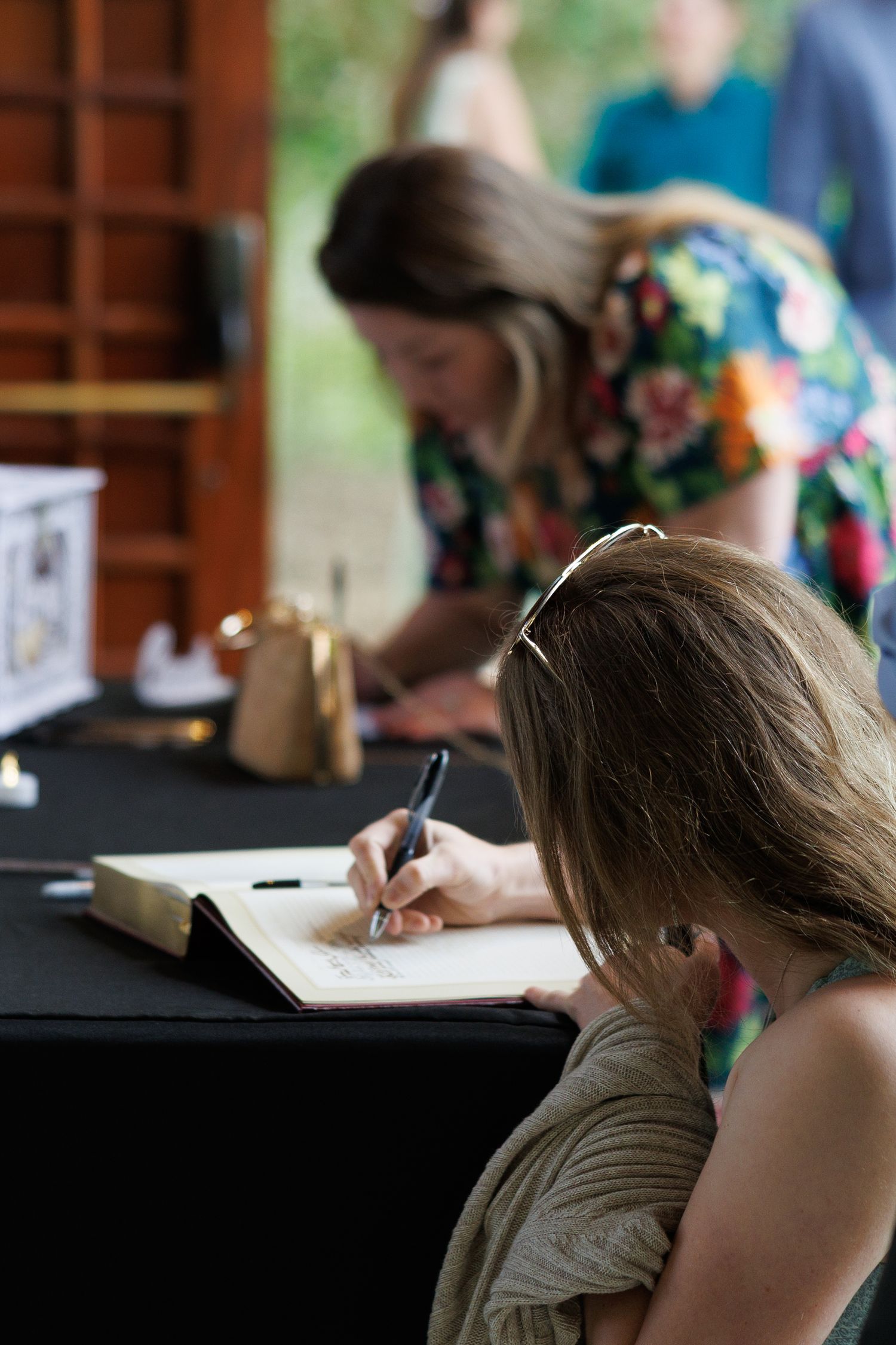 Woman signing a guest book at a wedding reception table with black tablecloth and gold decor.