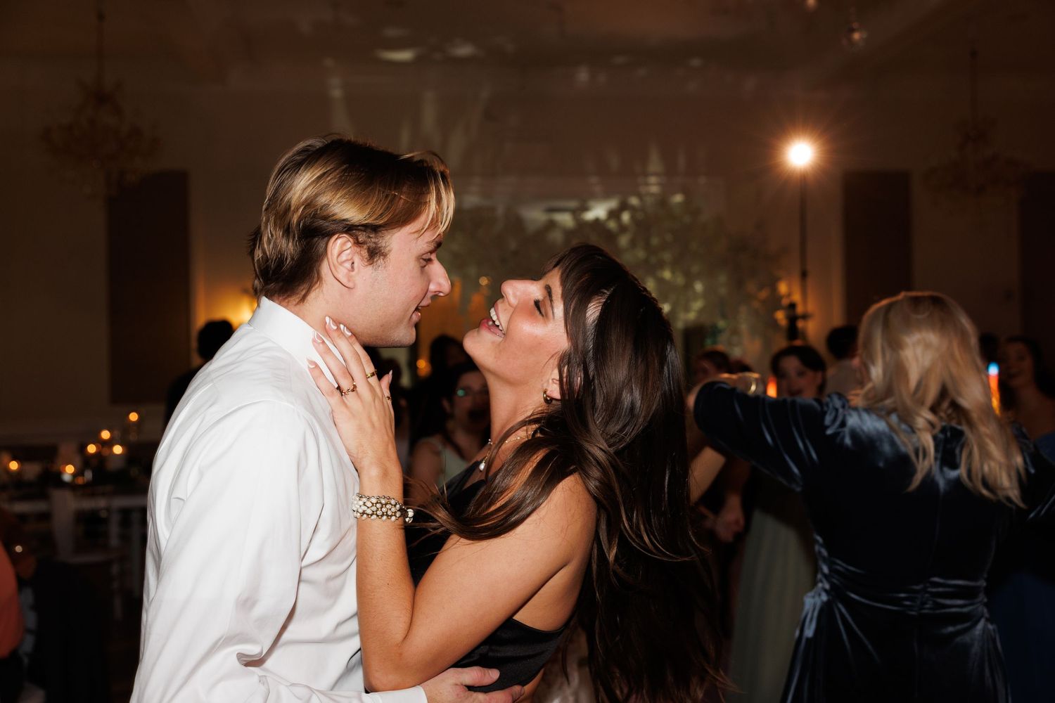 Couple shares a romantic slow dance embrace under warm lights at wedding reception.