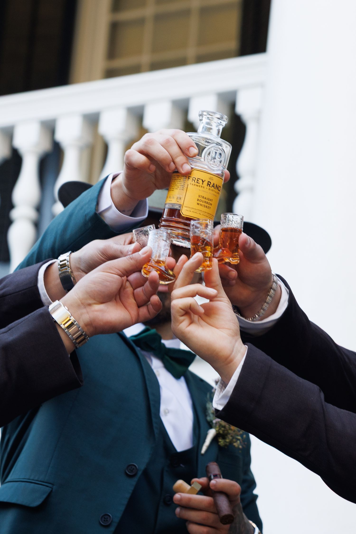 Groom and groomsmen in teal suits toasting with whiskey shots before the wedding ceremony.