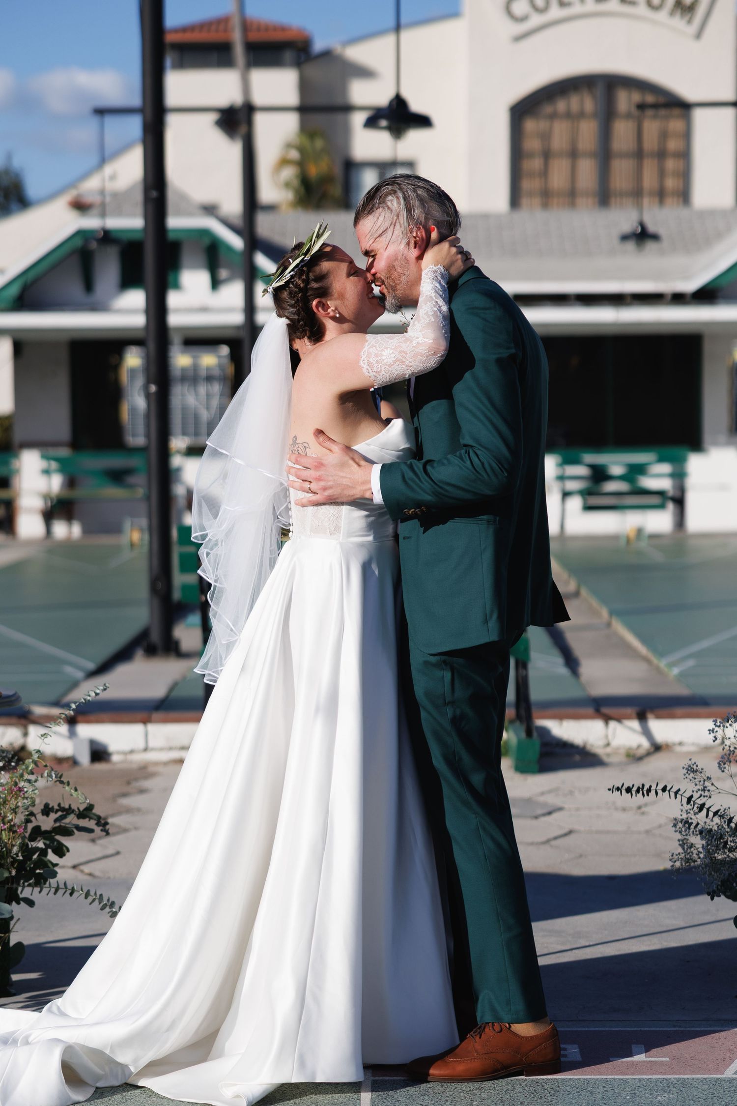Bride and groom sharing first kiss in front of a historic coliseum building on their wedding day.